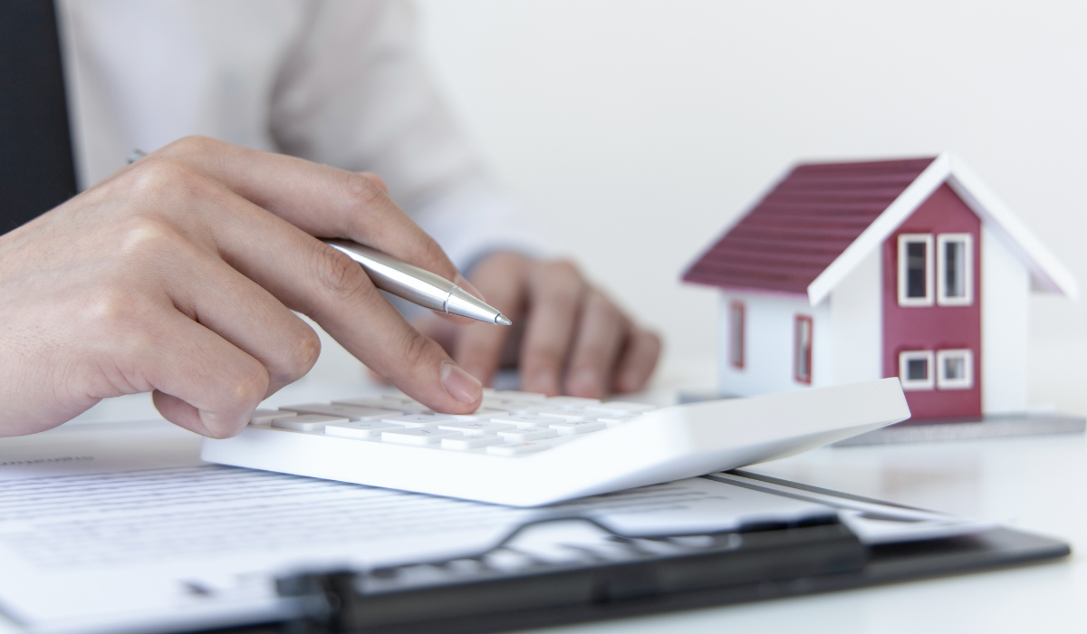 Person using a calculator near a model house and documents.