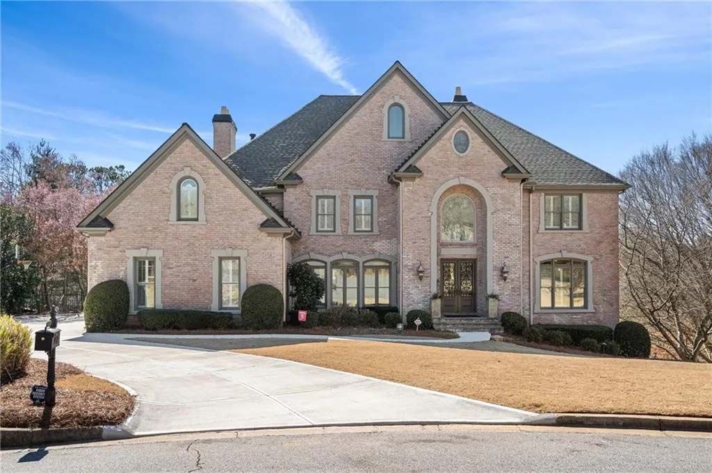 Large brick house with a long driveway under a blue sky.