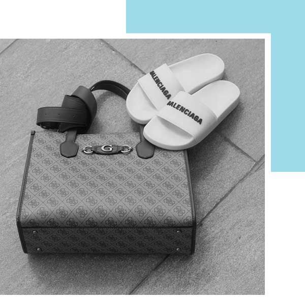 A handbag with a patterned exterior and a pair of white Balenciaga slides.