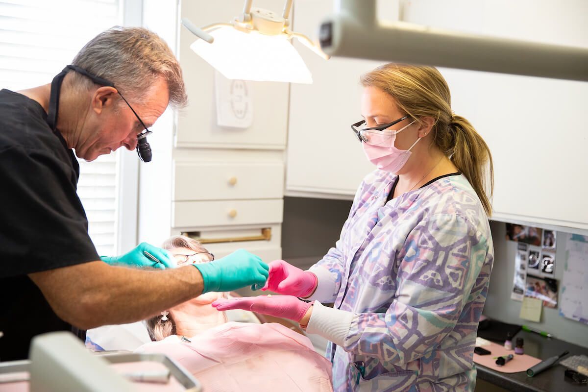 Dentist examining a patient's mouth with a dental assistant in a clinic.