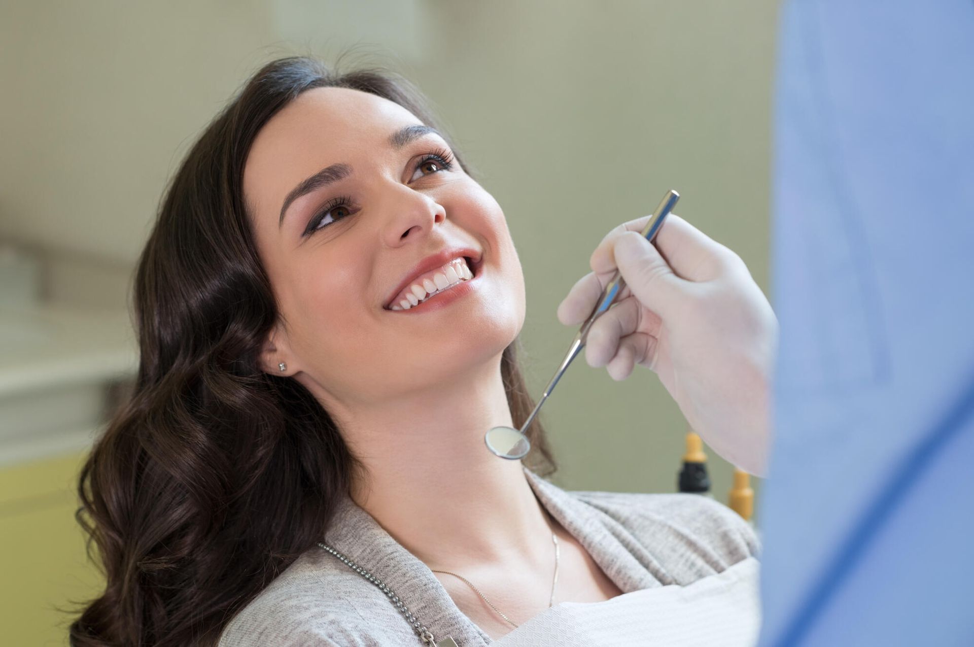 Woman smiles in dentist chair, dentist examines teeth with mirror and probe.
