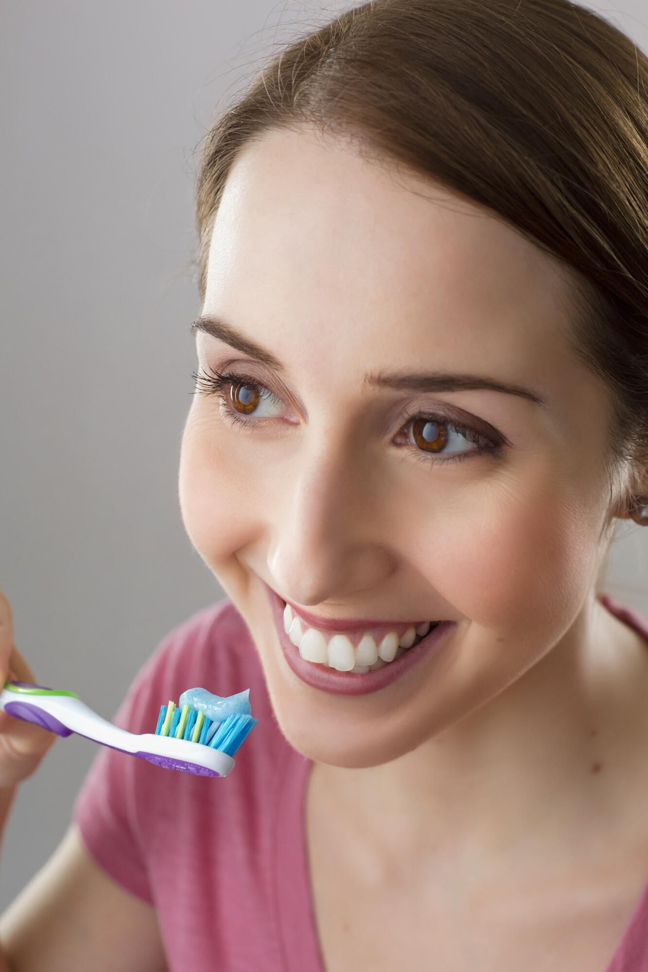 Smiling woman brushing her teeth with blue toothpaste on a white toothbrush