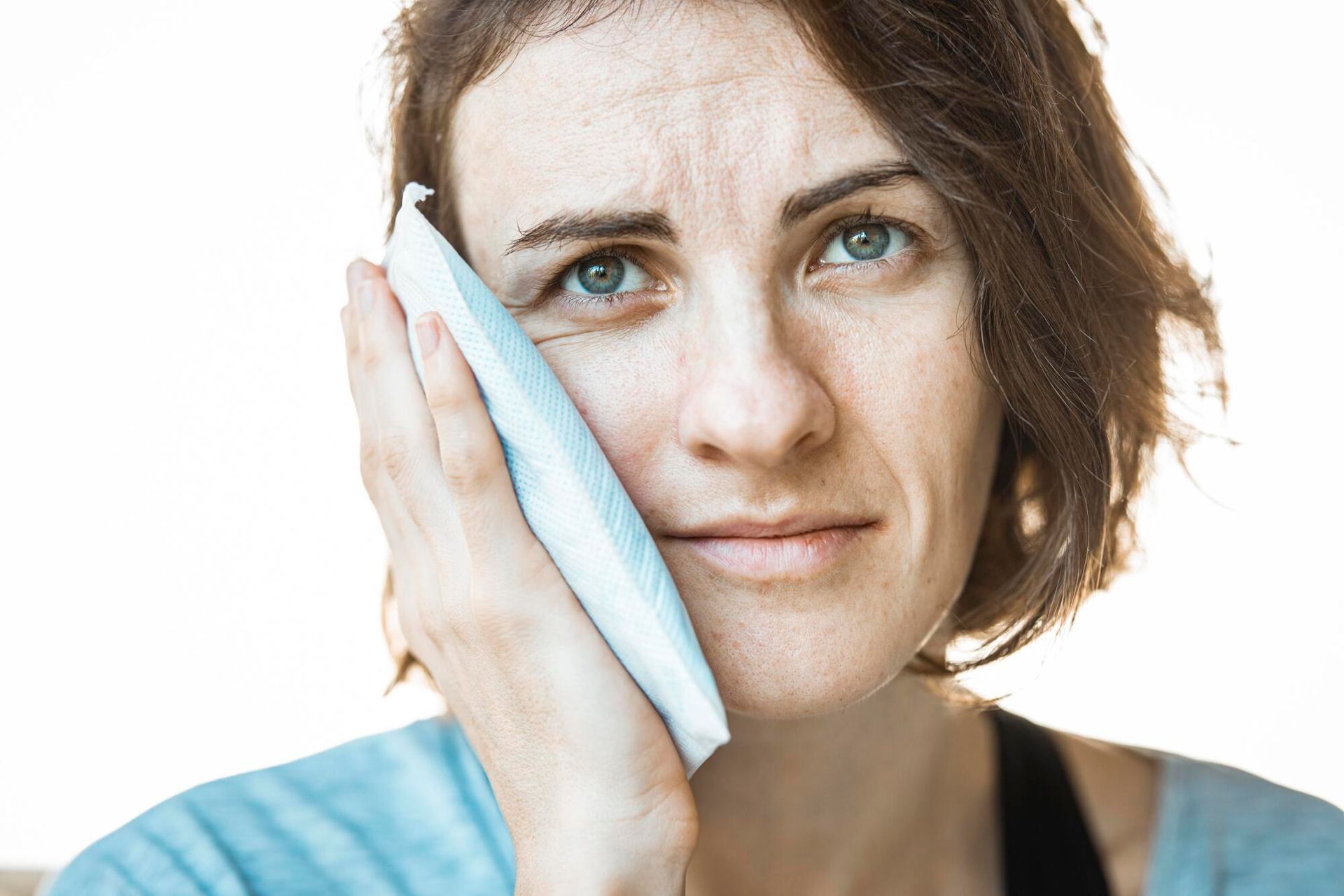 Woman holding a cold compress to her cheek, appearing pained.