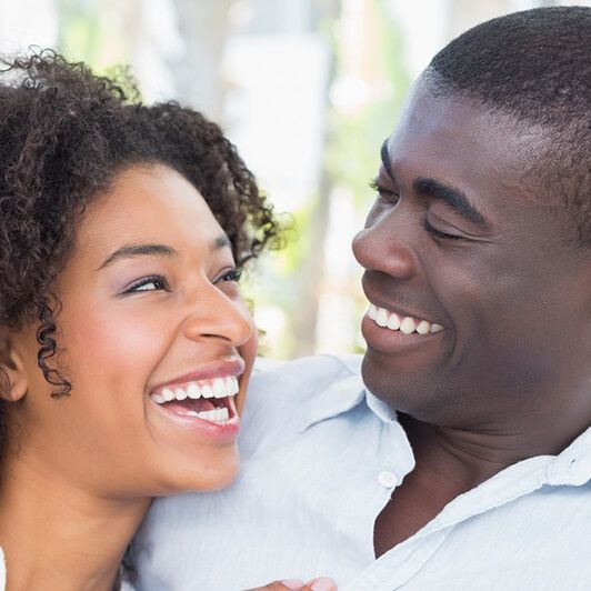Smiling Black couple, woman with curly hair, looking at each other, light background.