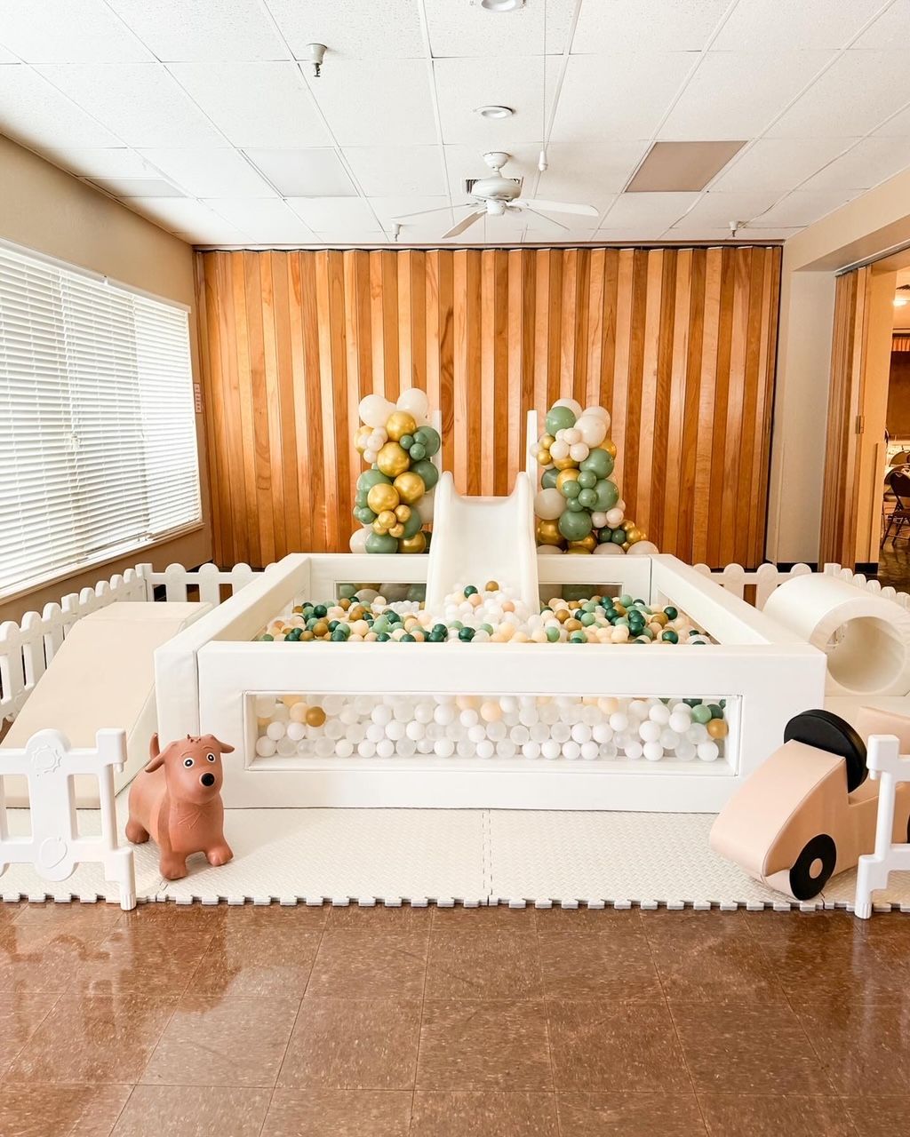 Pastel balloon-decorated party setup with white fencing, floral accents, and a wood-paneled backdrop