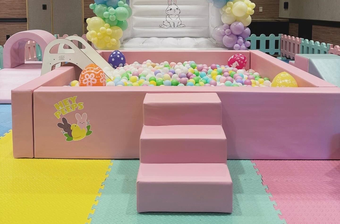 Pastel ball pit with pink steps, yellow and pink flooring, and a rainbow backdrop