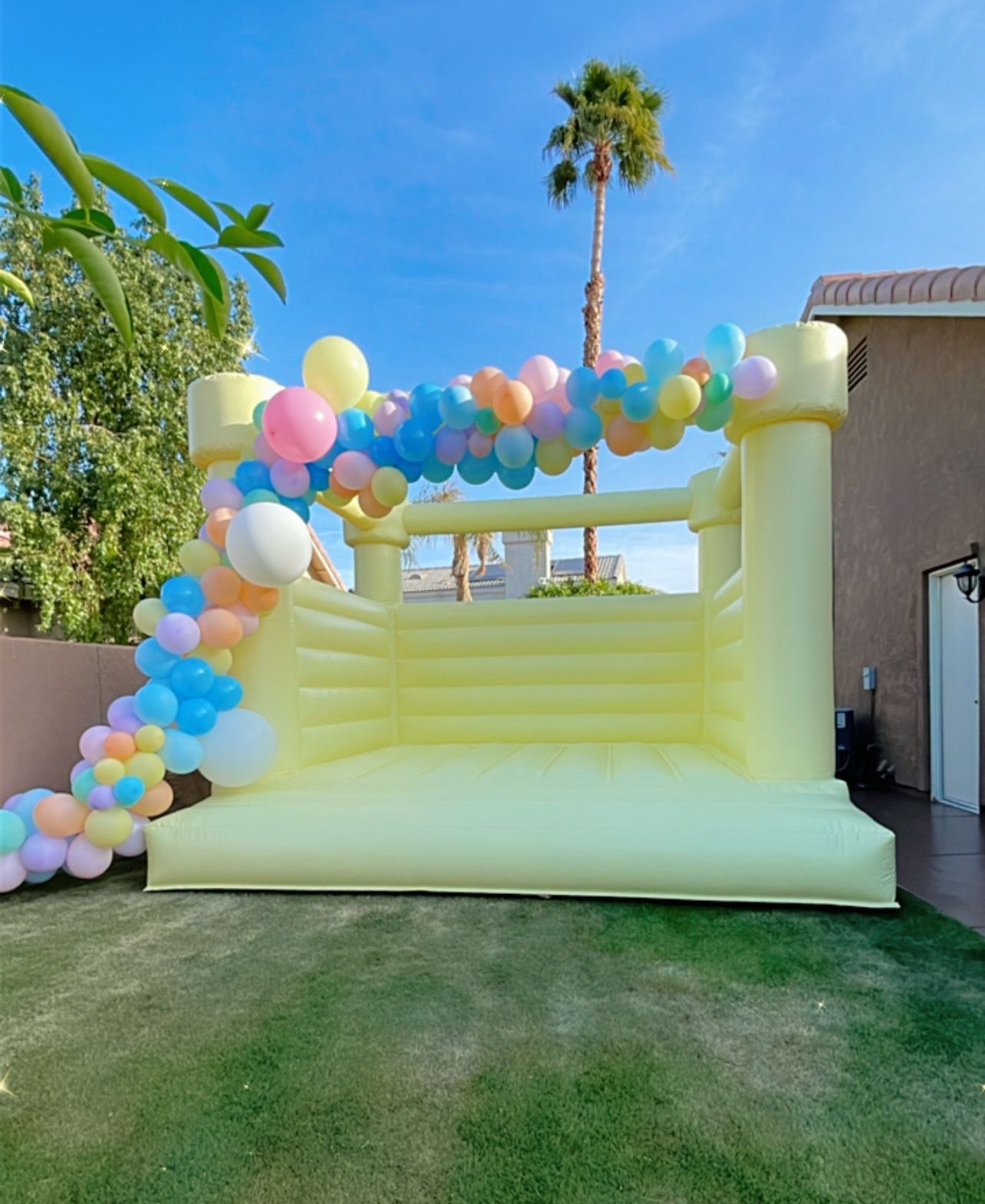 Colorful balloon arch over a yellow inflatable bounce house in a sunny backyard