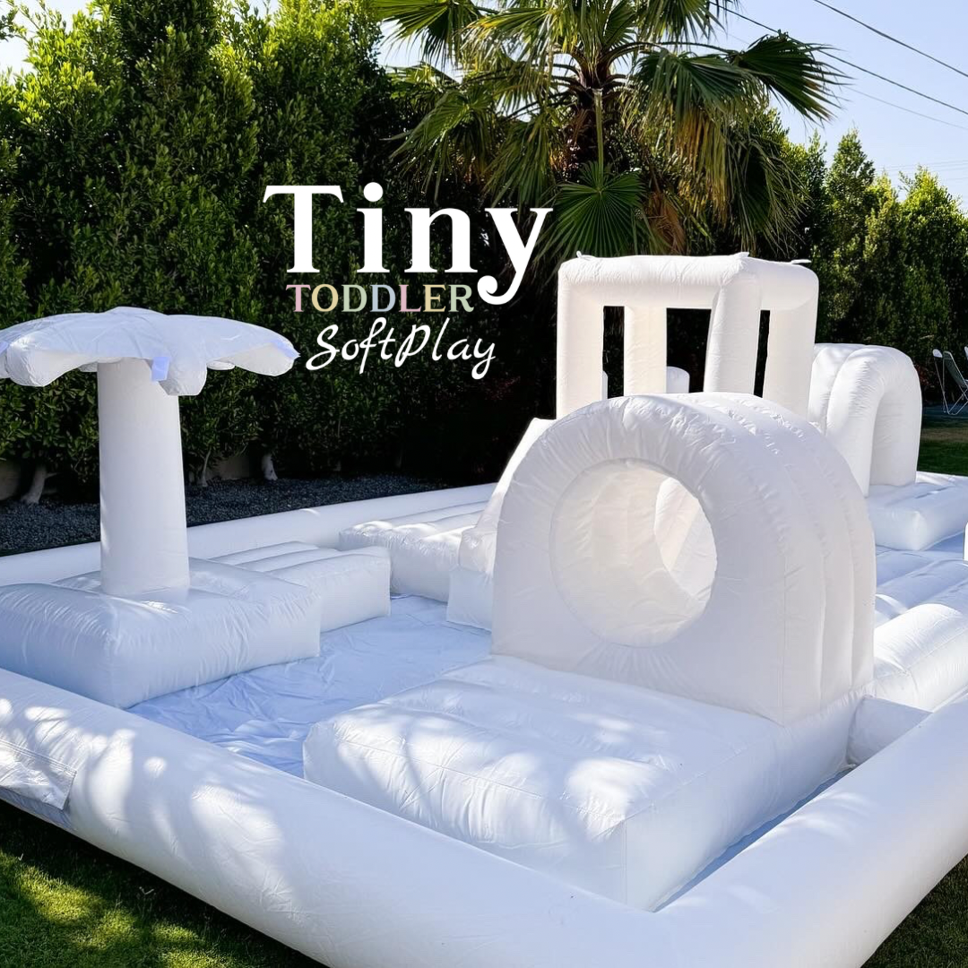 White inflatable toddler soft play set in a sunny outdoor yard with a small slide and tunnel.