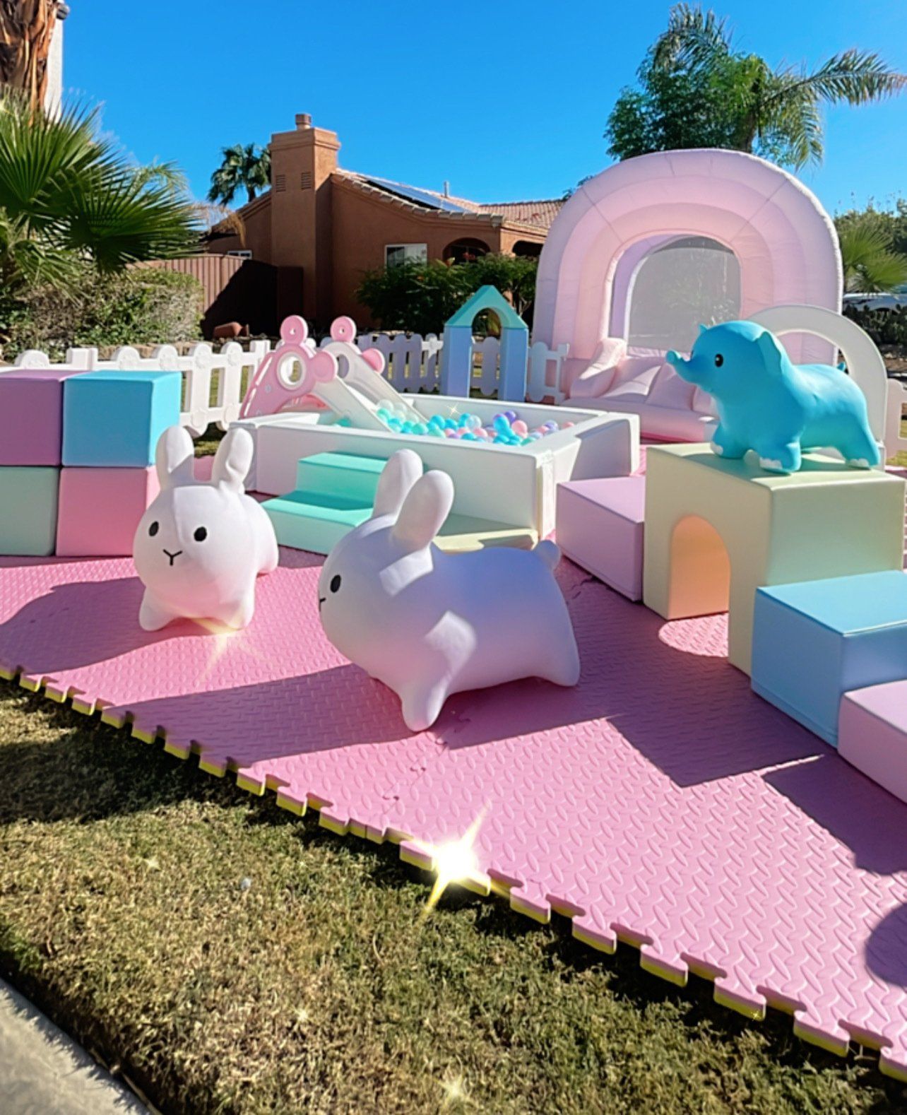 Pastel bunny playground with inflatable toys on a pink mat in a sunny backyard