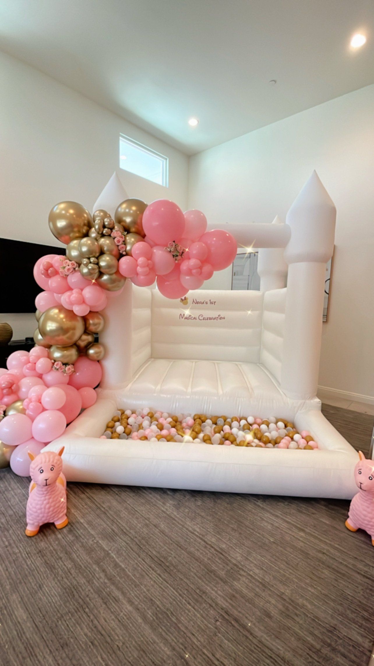 Pink and gold balloon castle bounce house in a room, with balloons along the entrance and base