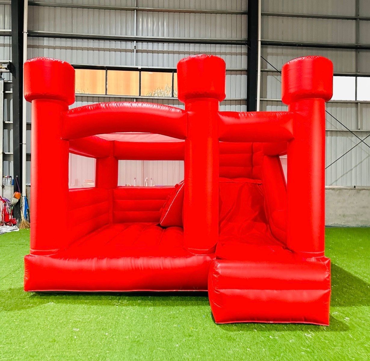 Red inflatable bounce house with slide inside a warehouse on green turf