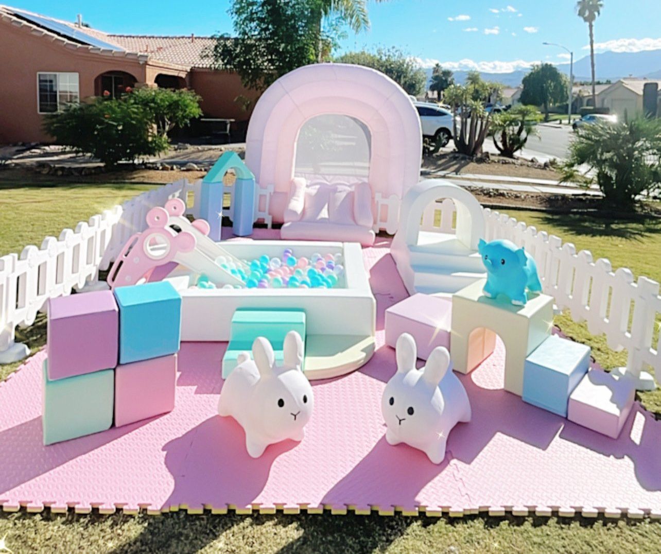 Pastel unicorn-themed bounce house with plush toys and blocks in a sunny yard