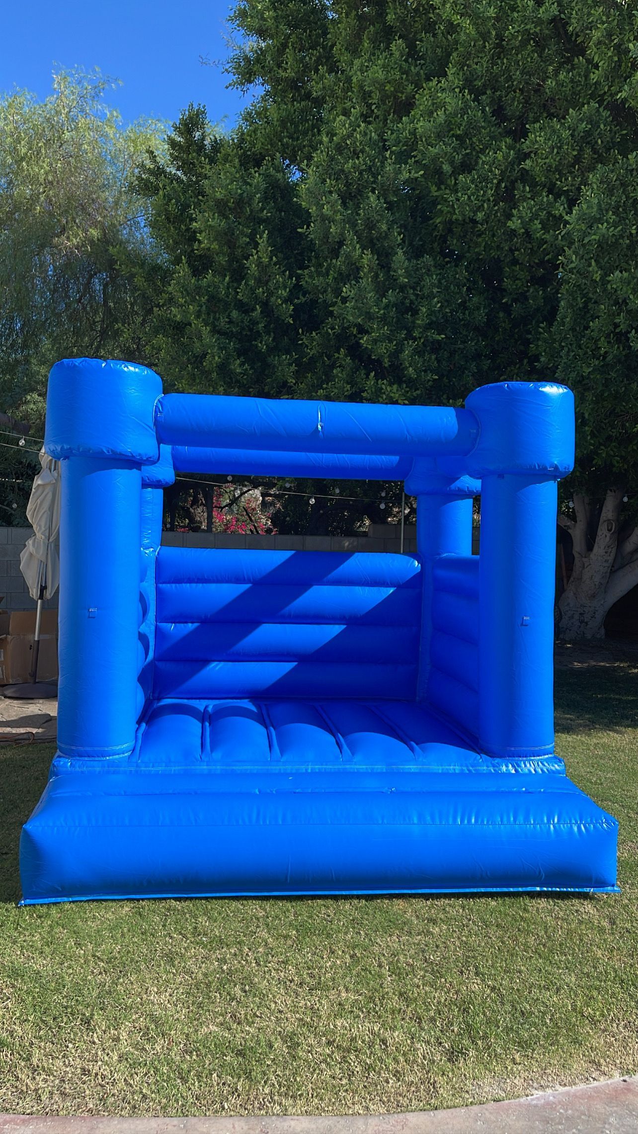 Blue inflatable bounce house on grass outdoors with trees in the background
