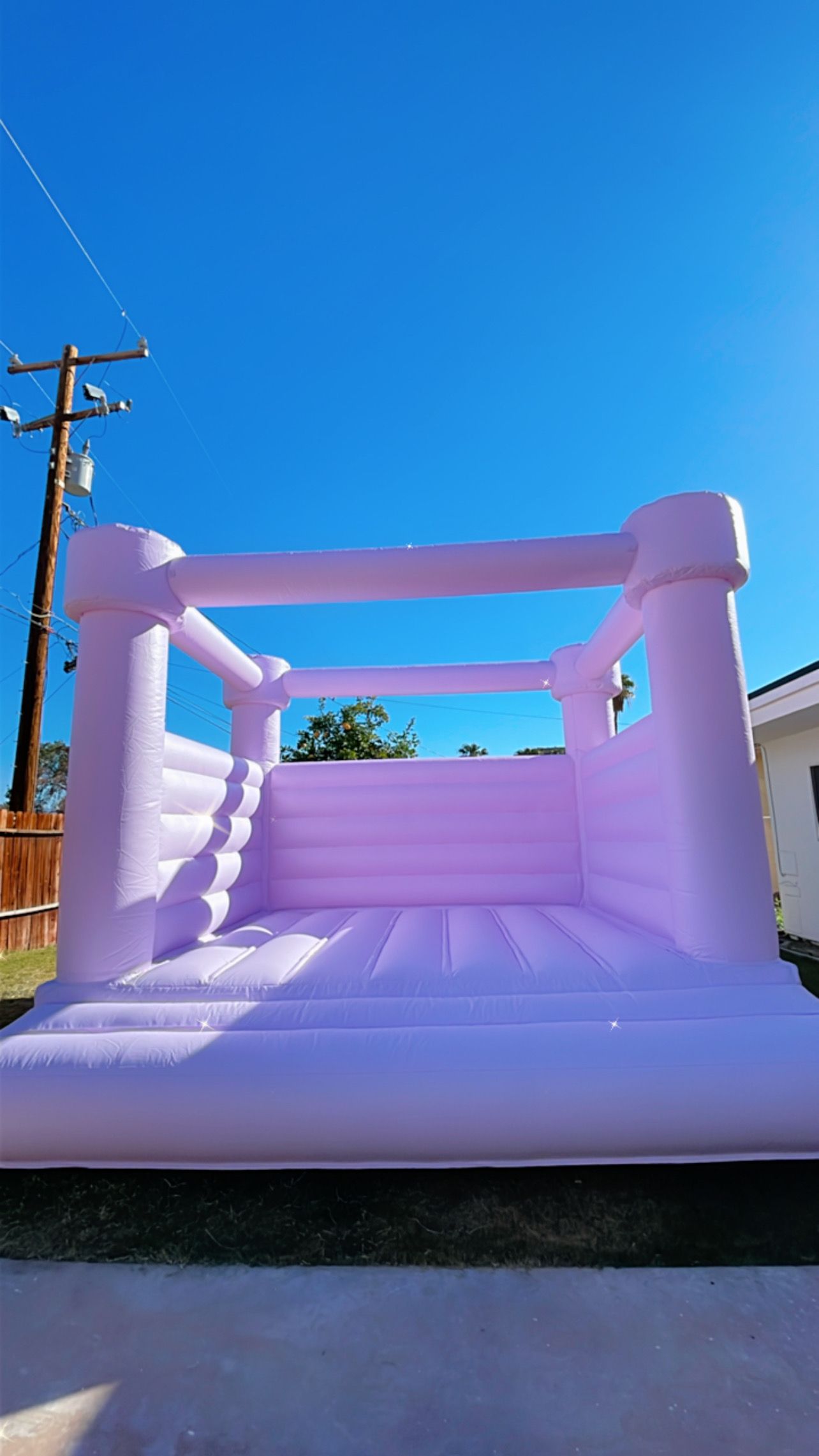 Pink inflatable bounce house in a driveway under a bright blue sky