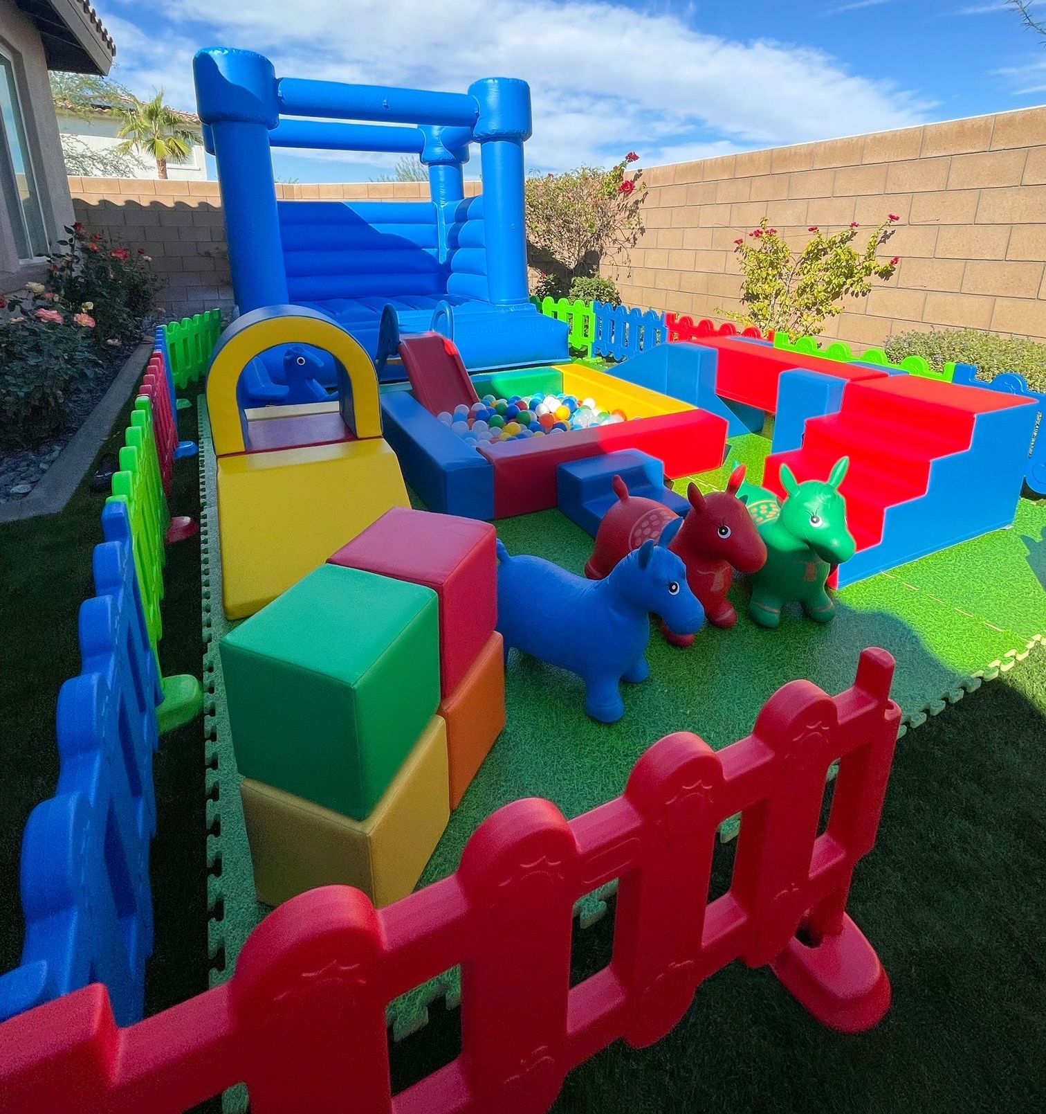 Colorful backyard toddler play area with inflatable bounce house, soft blocks, and plastic animal toys