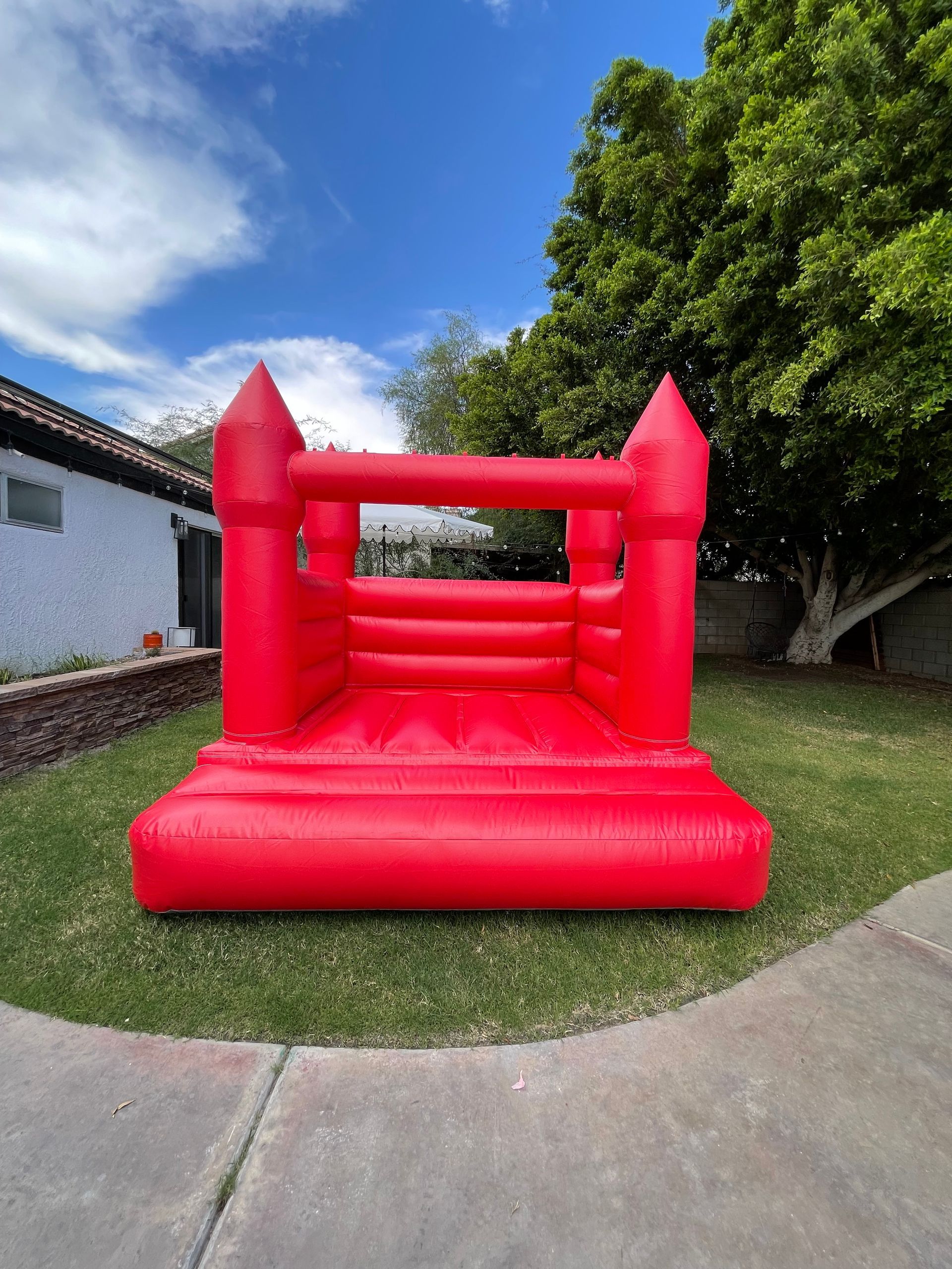 Red inflatable bounce house on a grassy lawn beside a sidewalk and trees
