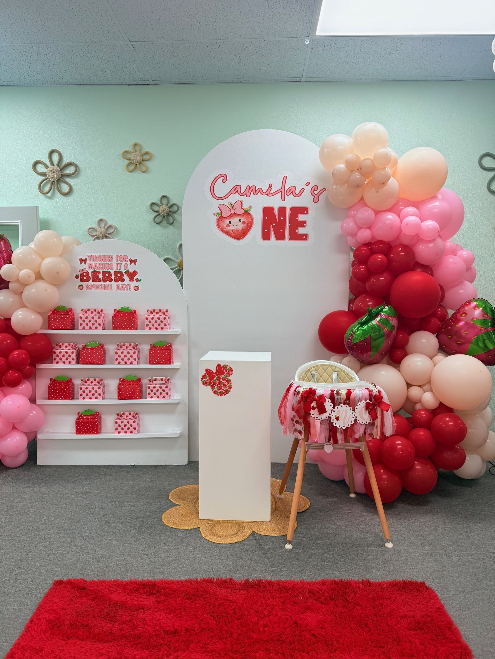 Pink-and-white birthday balloon display with cake stands and a red carpet in a decorated room