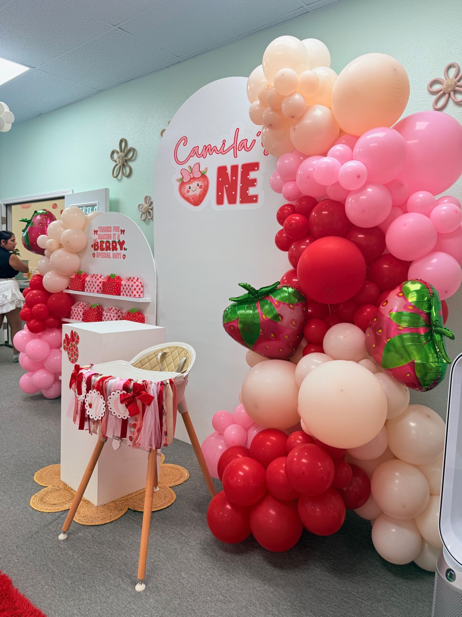Pink and red balloon arch beside a decorated dessert table in a celebration room