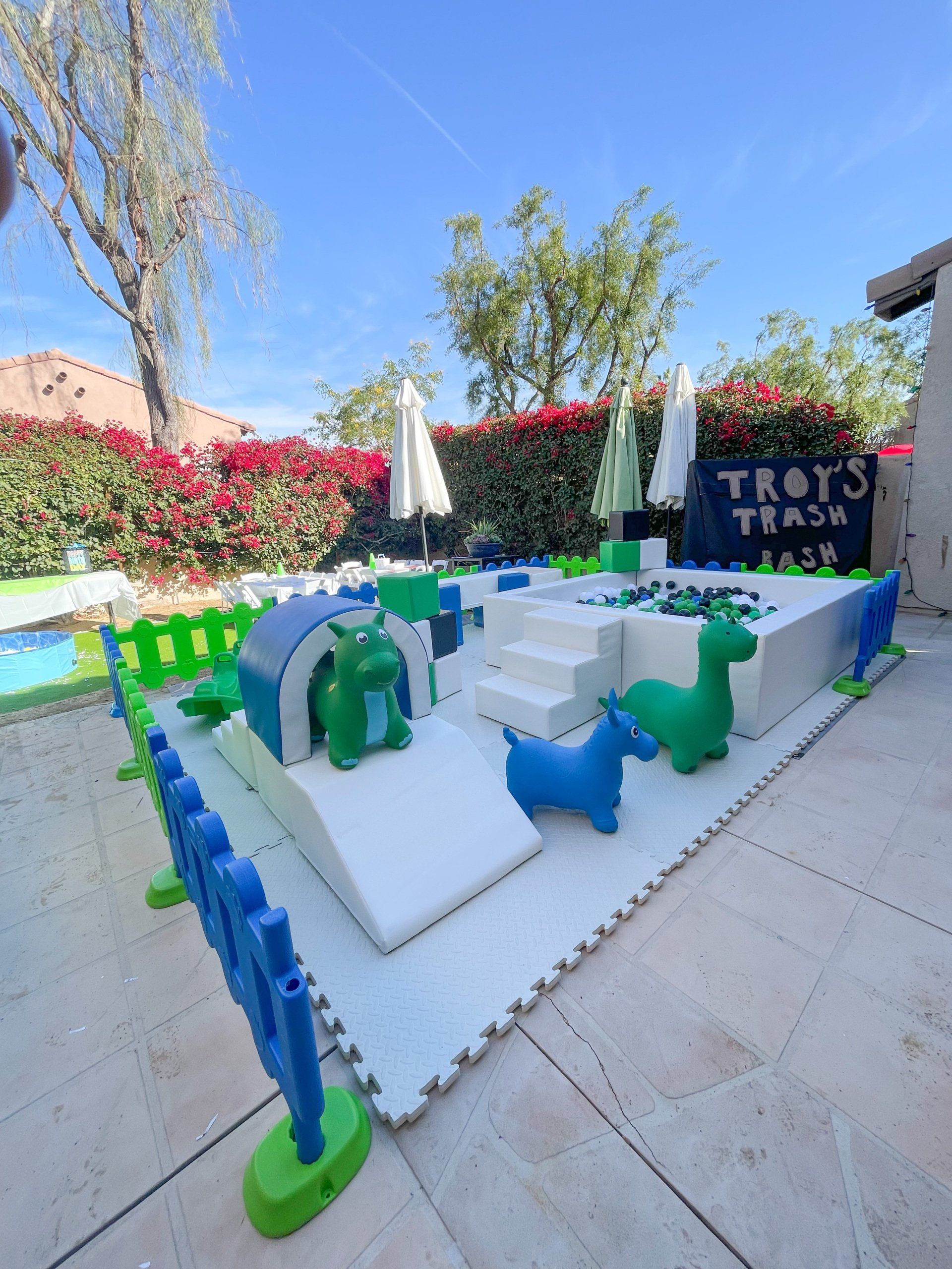 Outdoor tabletop game setup with green and blue pieces on a white board beside a “TROIS TEAM” sign.