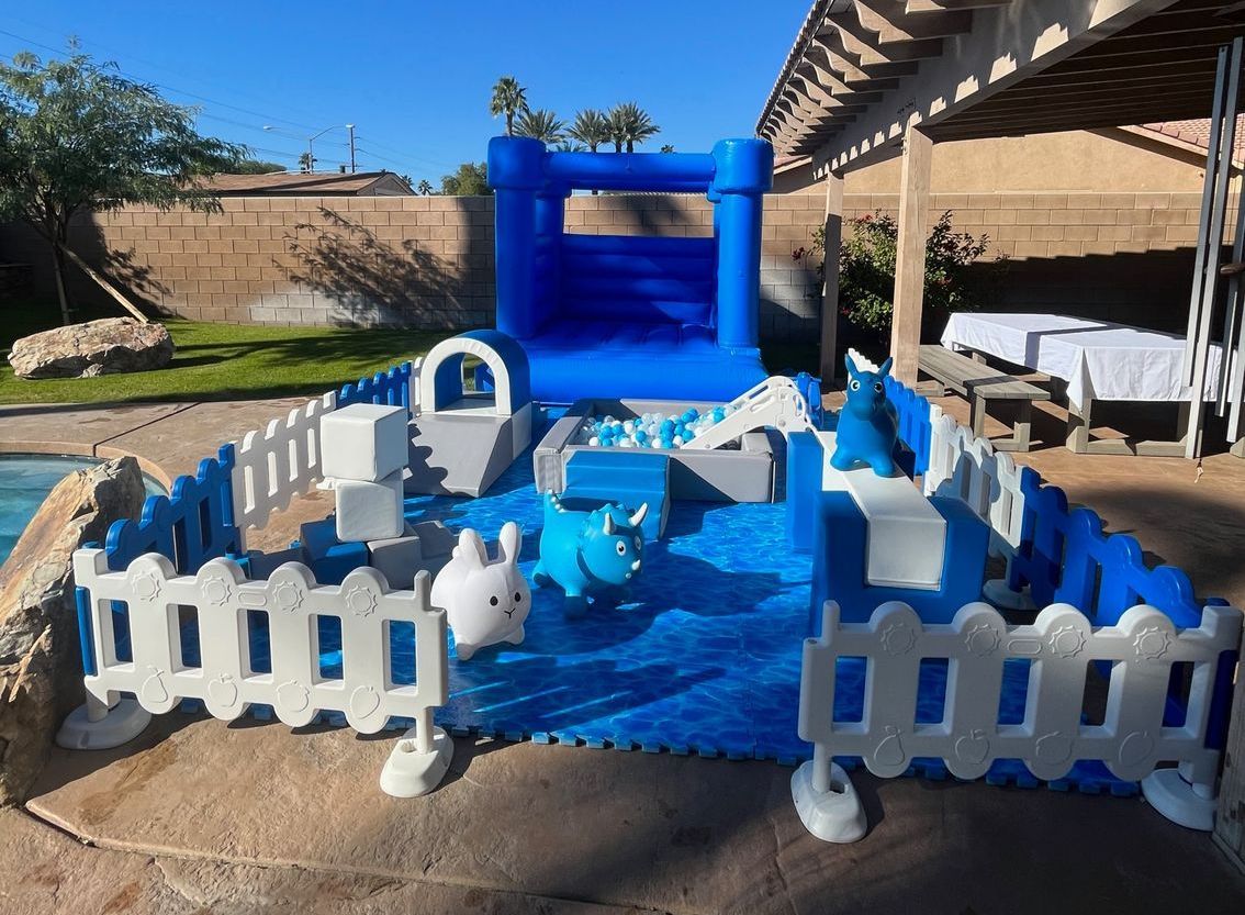 Blue inflatable backyard water slide with a fenced splash area and pool toys, set in a sunny yard