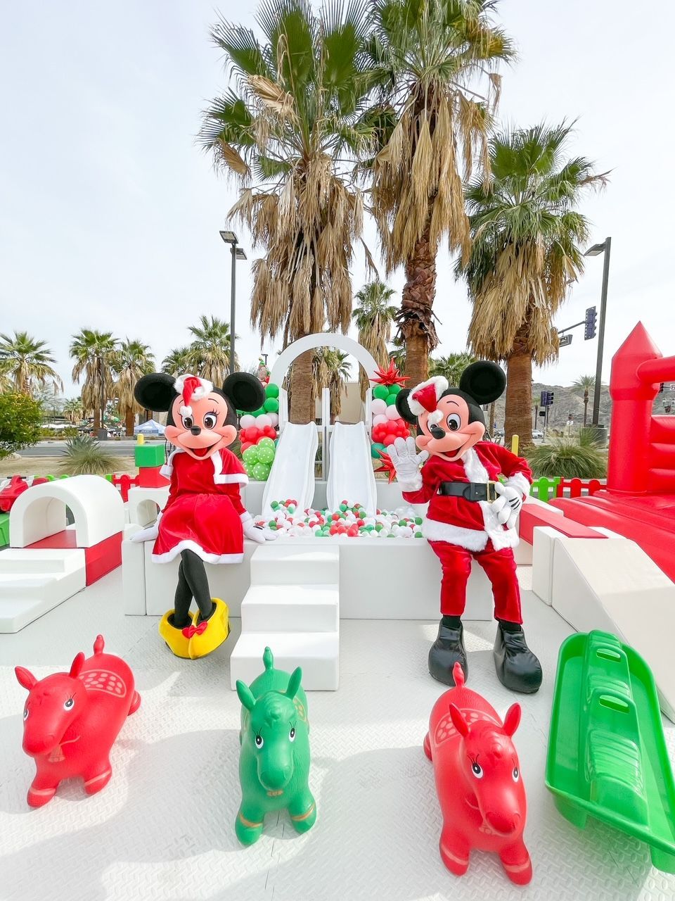 Mickey and Minnie mouse statues in red outfits on a white outdoor display with palm trees and colorful animal figures