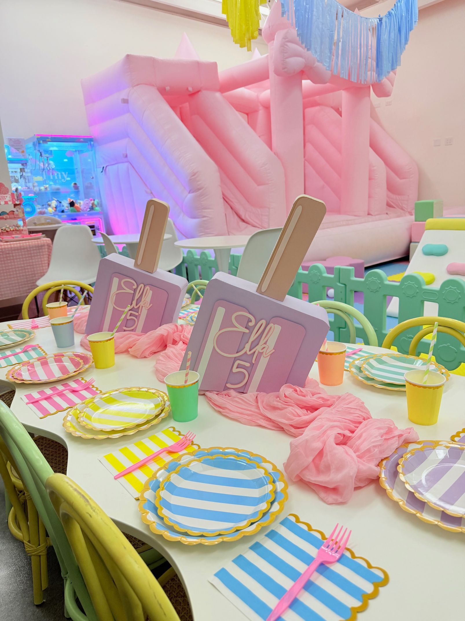 Pastel candy-themed party table with colorful plates, drinks, and pink balloon decor