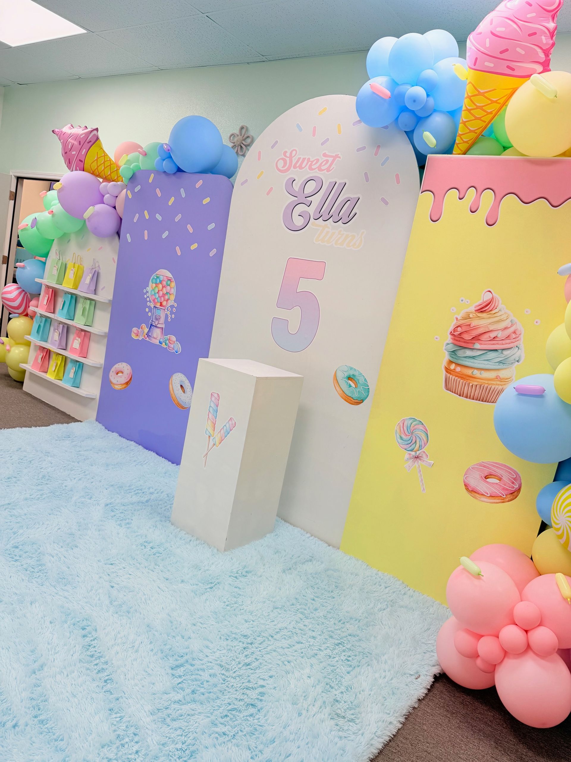 Colorful unicorn-themed birthday party backdrop with balloons, cupcakes, and a large “5” sign