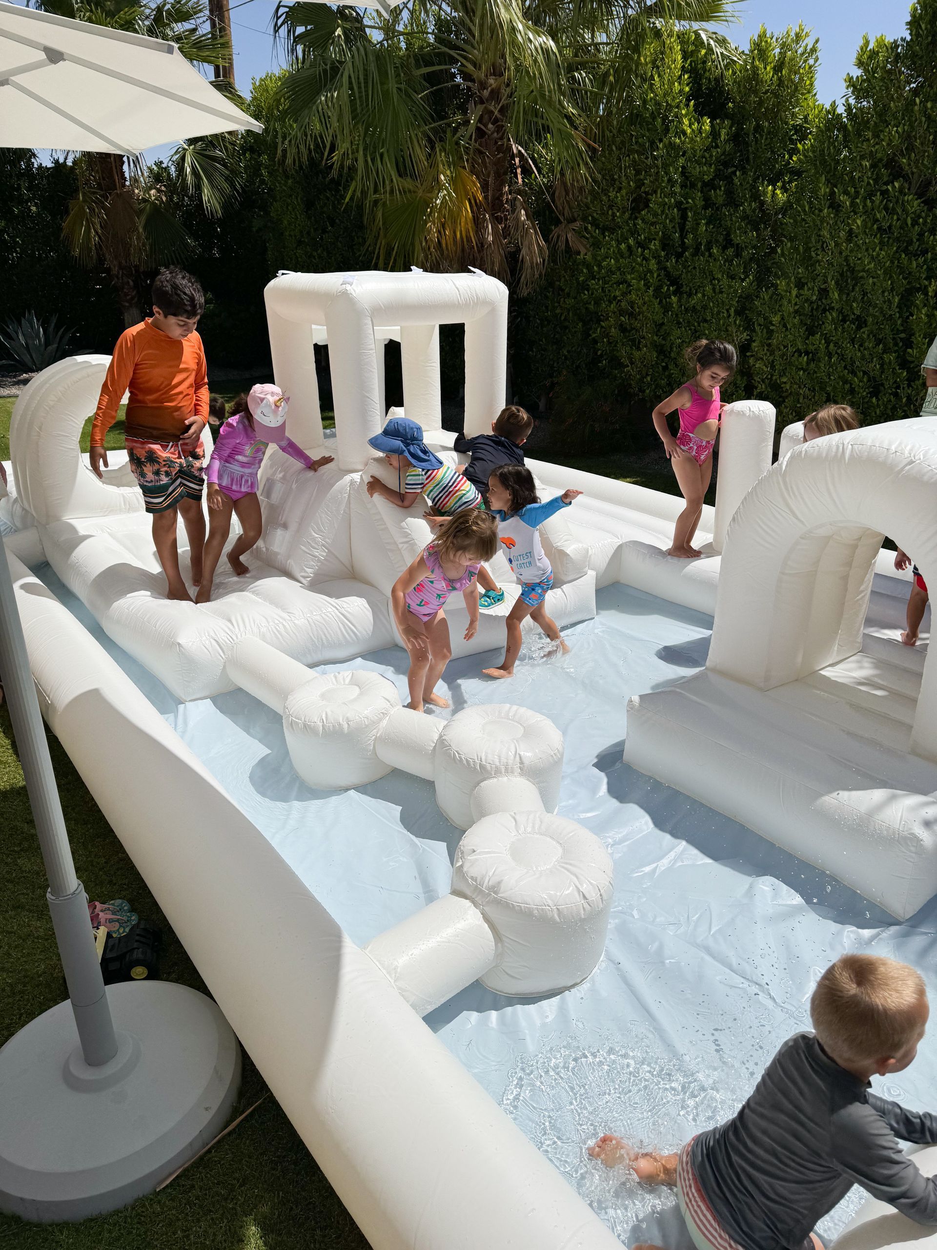 Children playing in a white inflatable water bounce house with shallow water outdoors