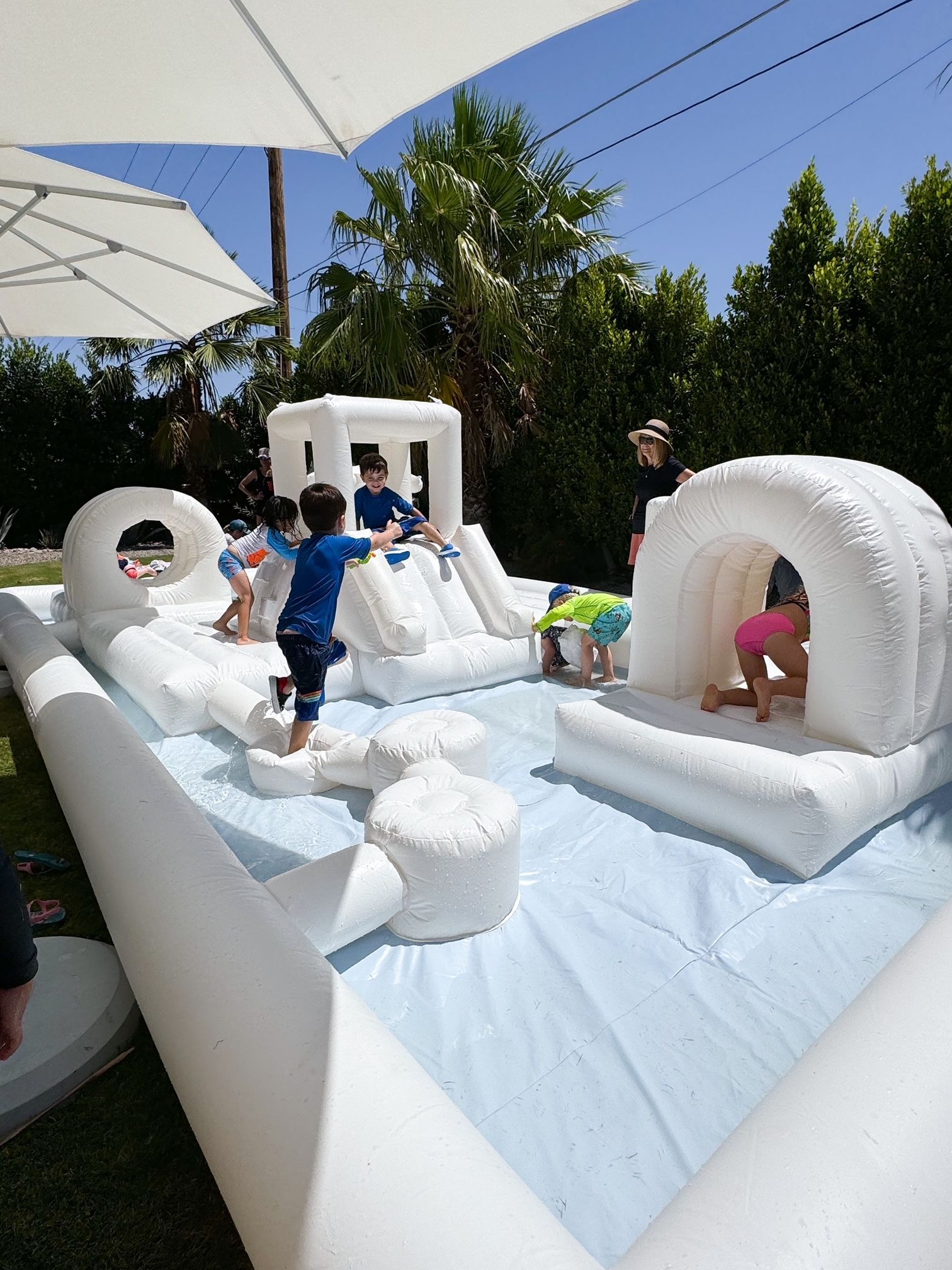 Children playing on a white inflatable bounce house with blue floor outdoors under a sunny sky