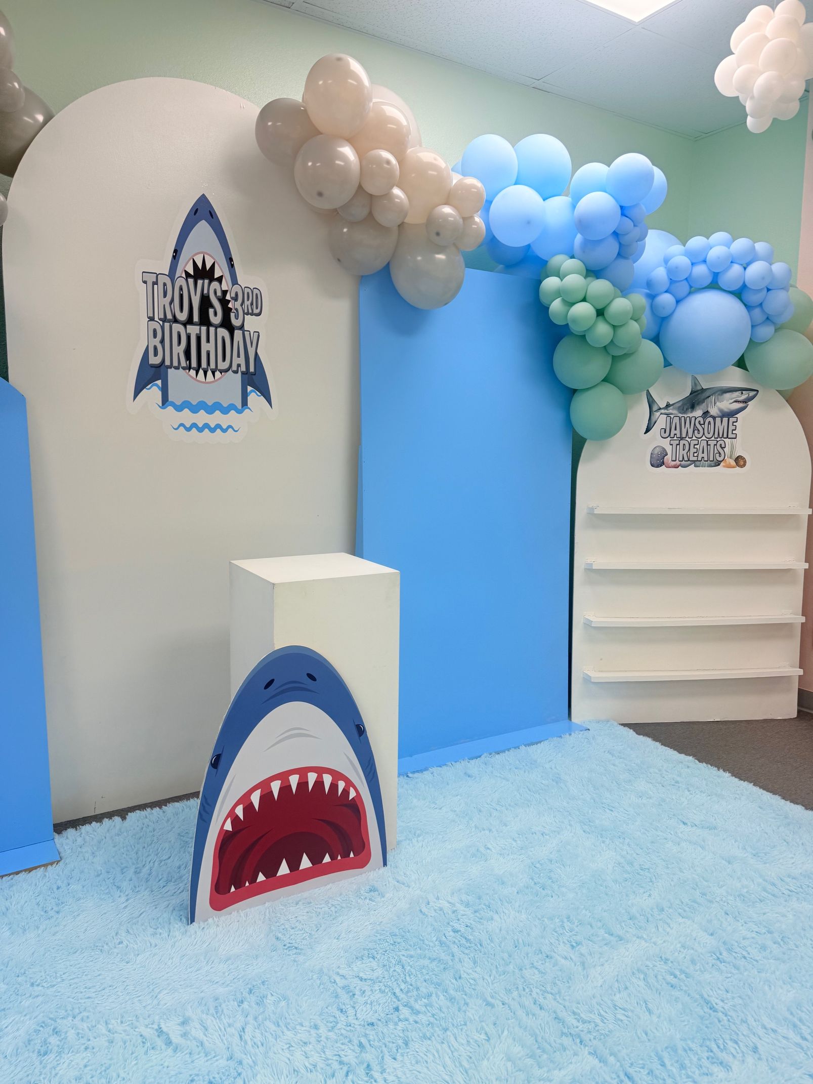 Blue birthday party setup with balloon arch, shark prop, and “Happy Birthday” decorations