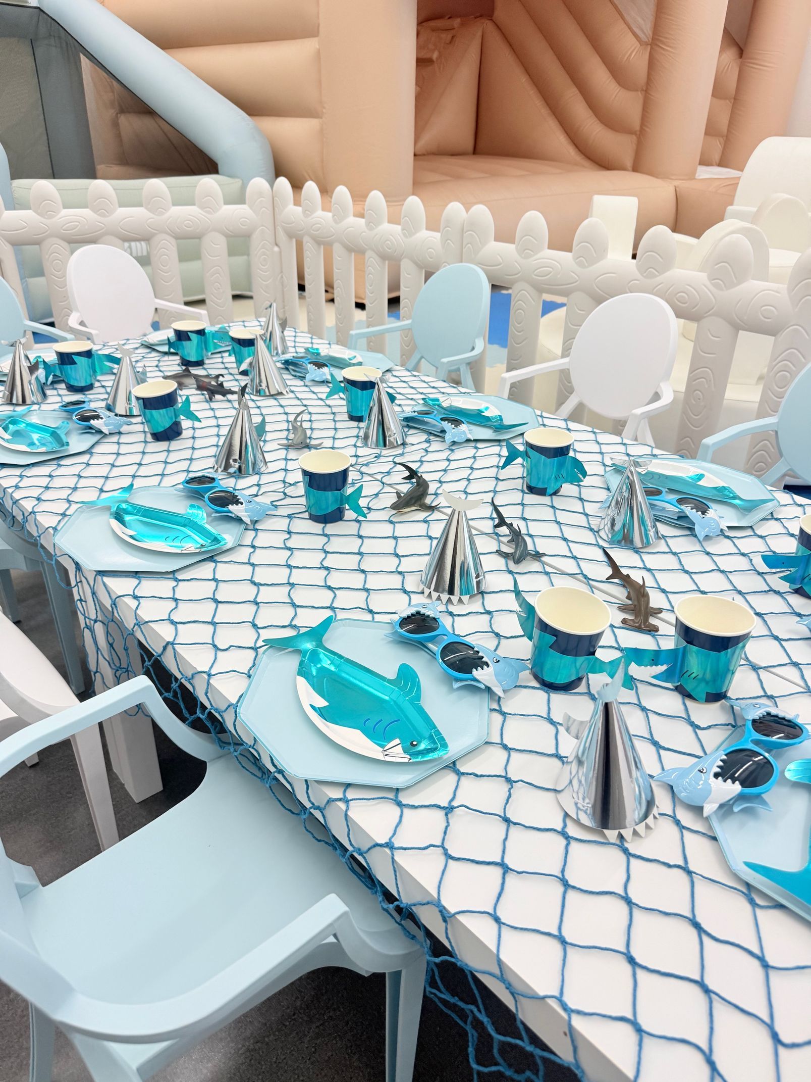 Outdoor table set with white chairs, blue net tablecloth, and turquoise plates with glassware and candles