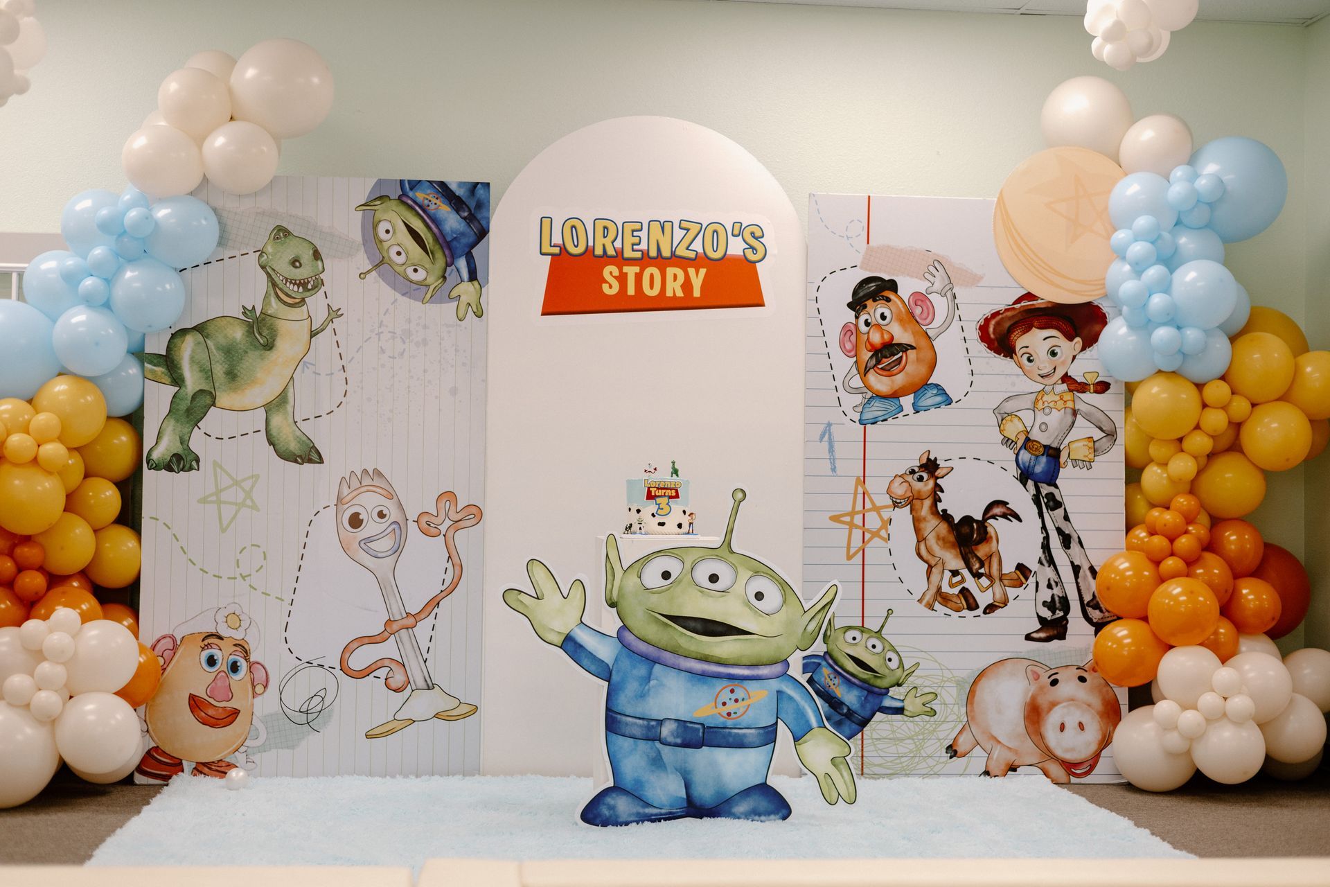 Toy Story-themed birthday backdrop with balloon arches and cartoon character cutouts around a central sign