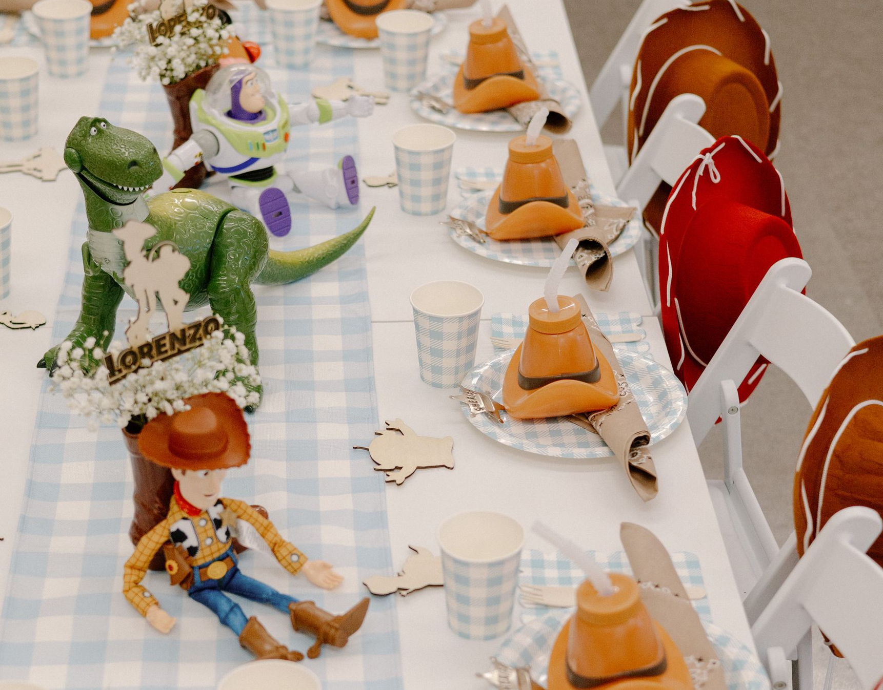 Toy Story character table setting with cowboy and dinosaur figures, orange napkins, and checkered tablecloth