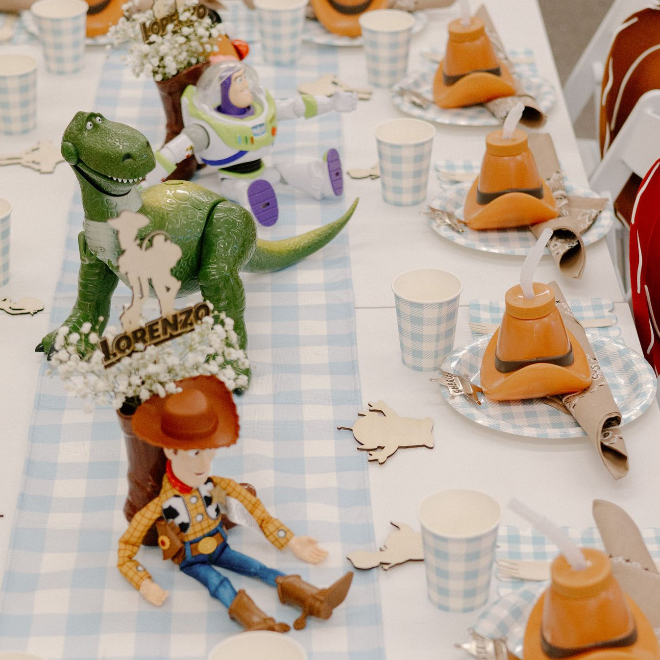 Toy Story character figurines on a checkered party table with orange dessert cups and paper plates
