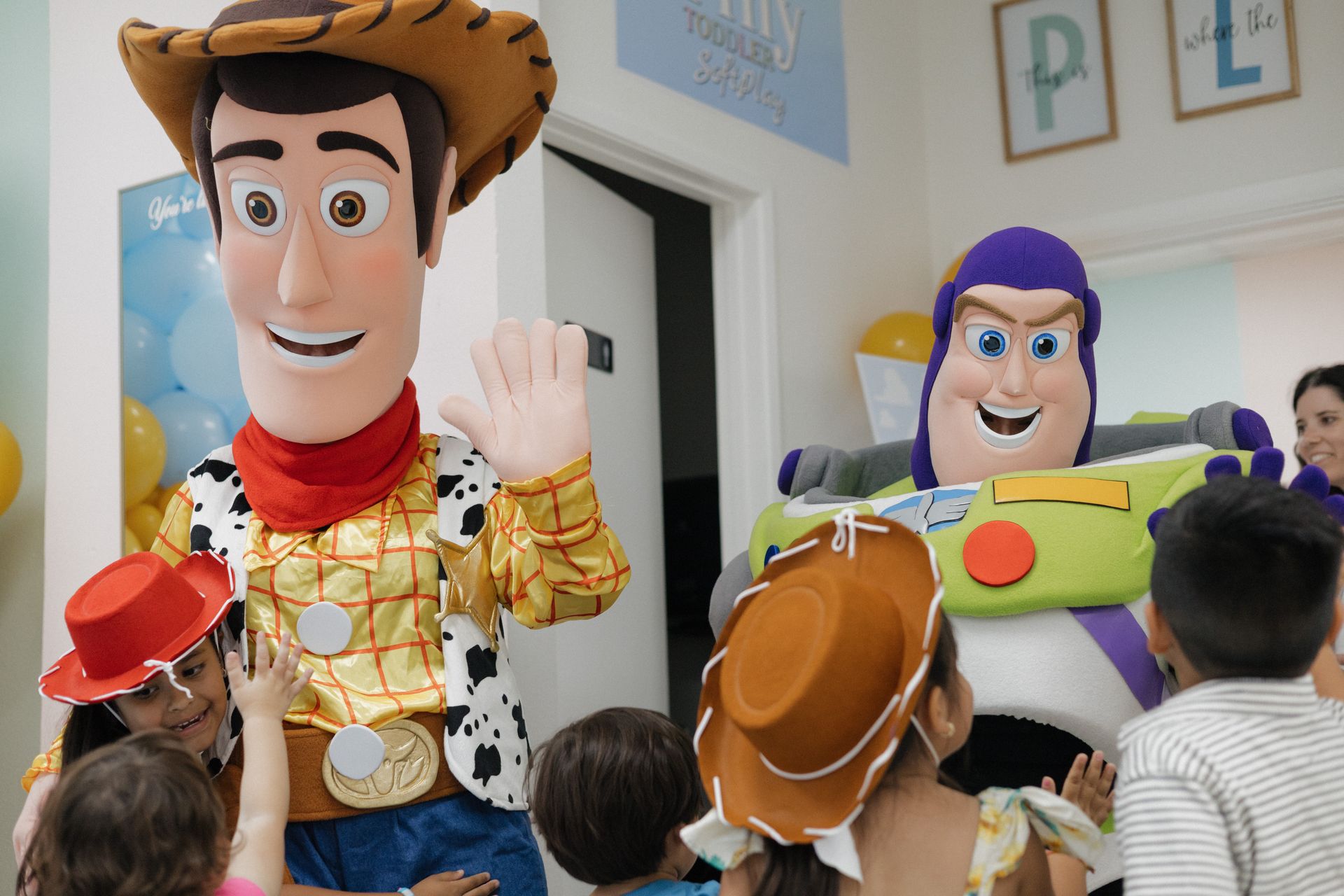 Two large Toy Story character mascots greeting children indoors