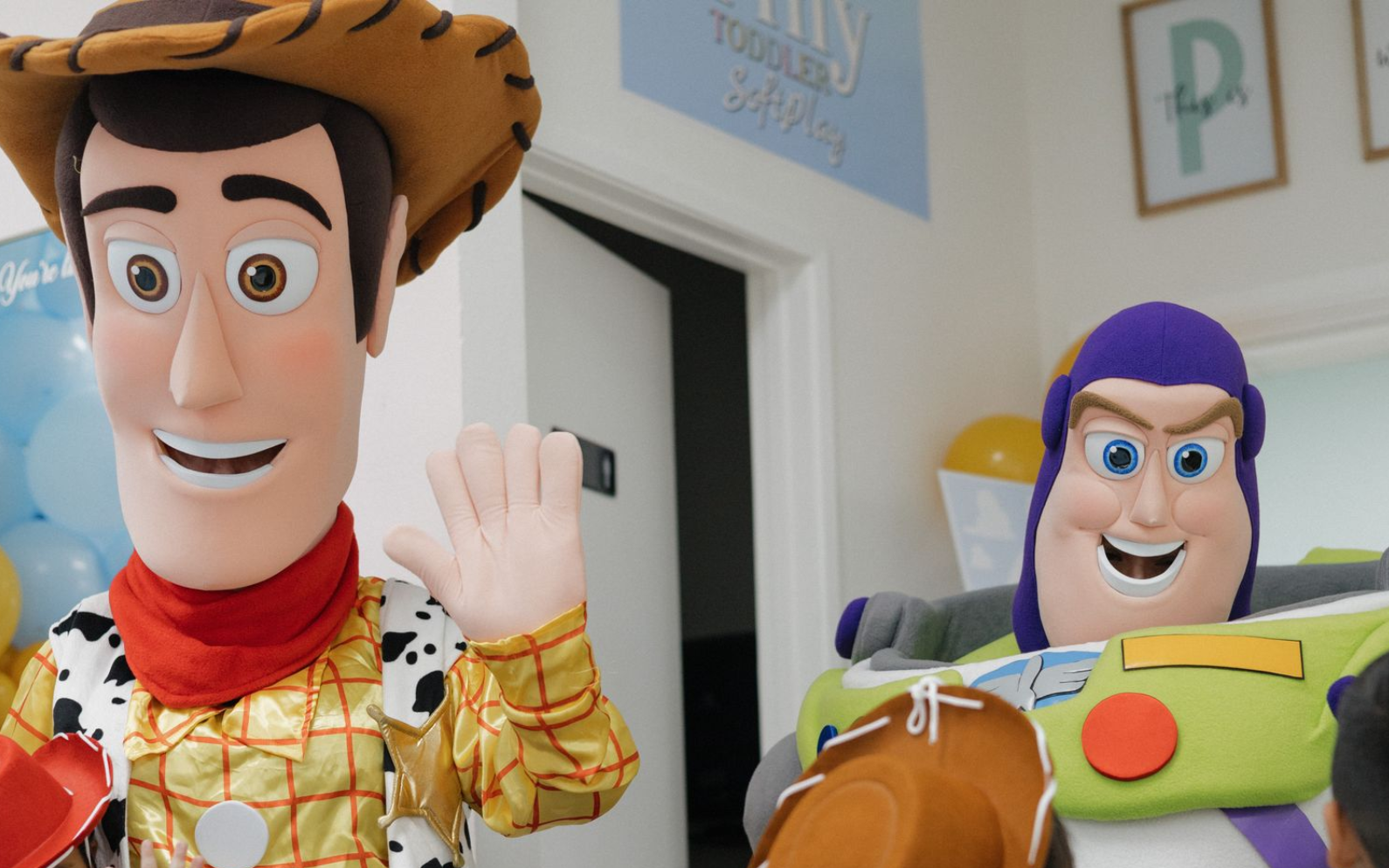 Toy cowboy and astronaut figures smiling indoors, one waving at the camera.