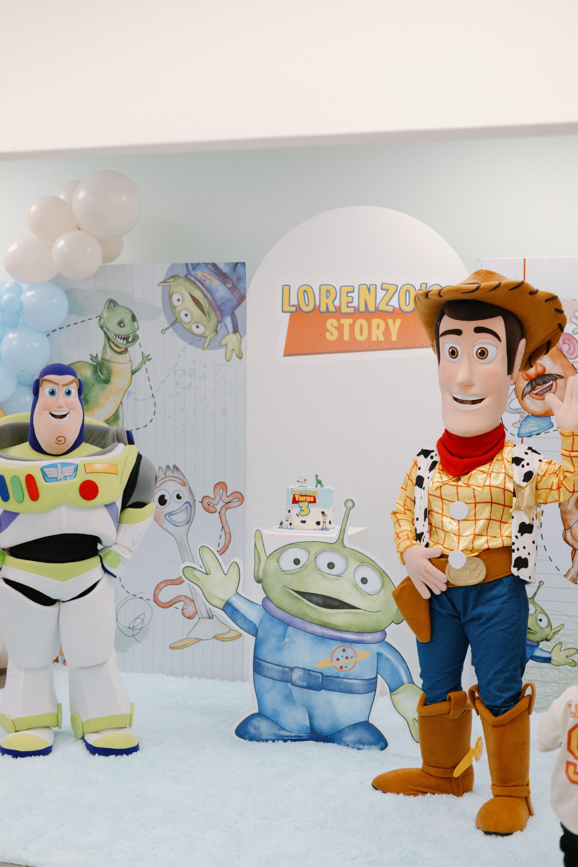 Buzz Lightyear and Woody standing beside a green alien at a Toy Story display.