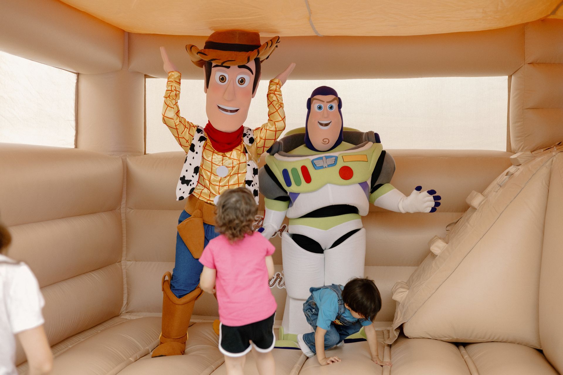 Woody and Buzz Lightyear in an inflatable bounce house with two small children looking up