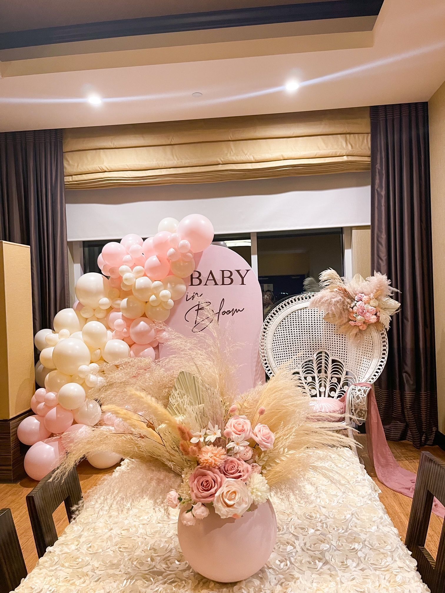 Pastel baby shower backdrop with balloons, floral arrangements, and a “BABY” sign indoors