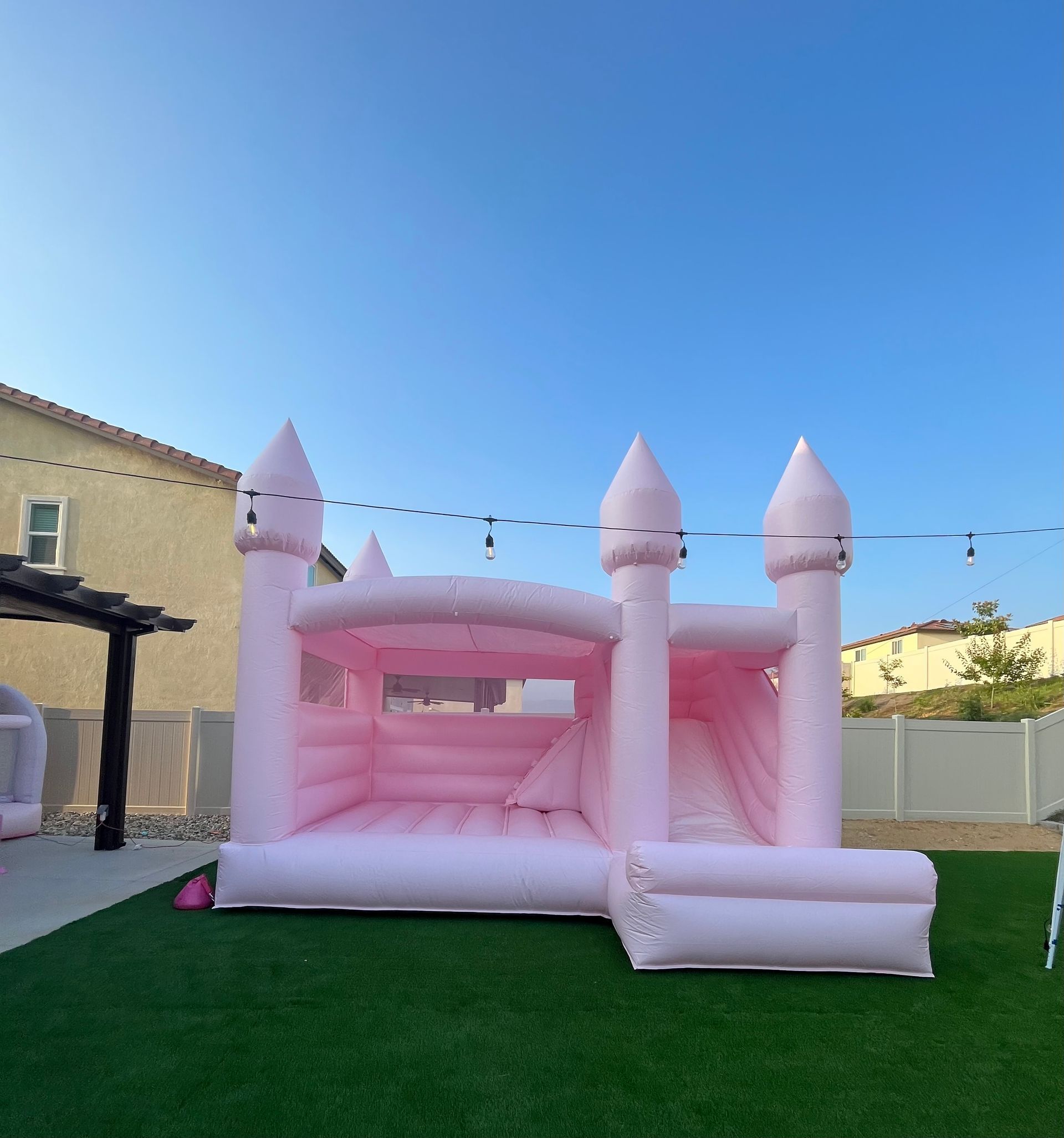 Pink castle bounce house on a green lawn in a sunny backyard.