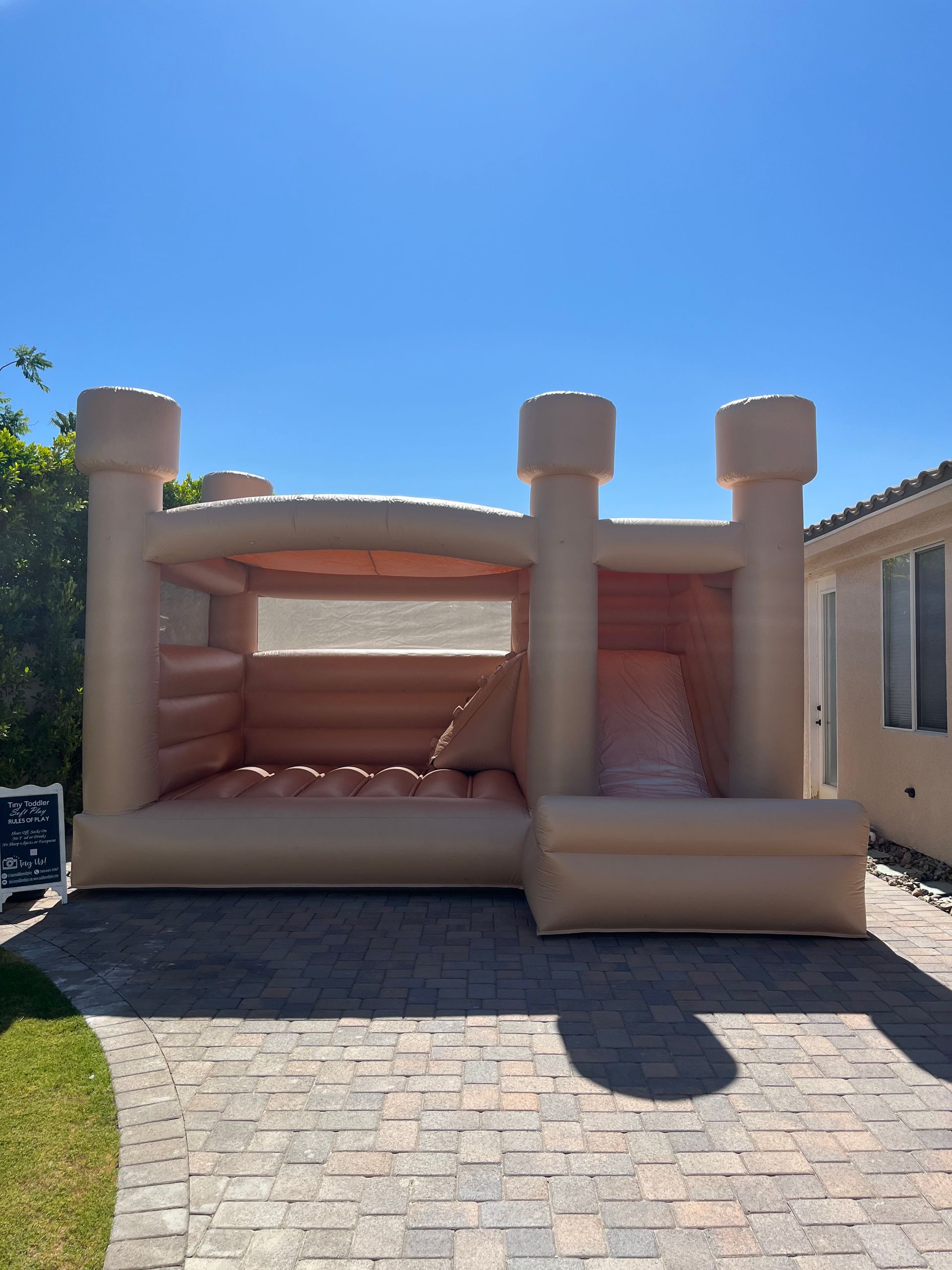 Beige inflatable bounce house in a sunny driveway with blue sky overhead