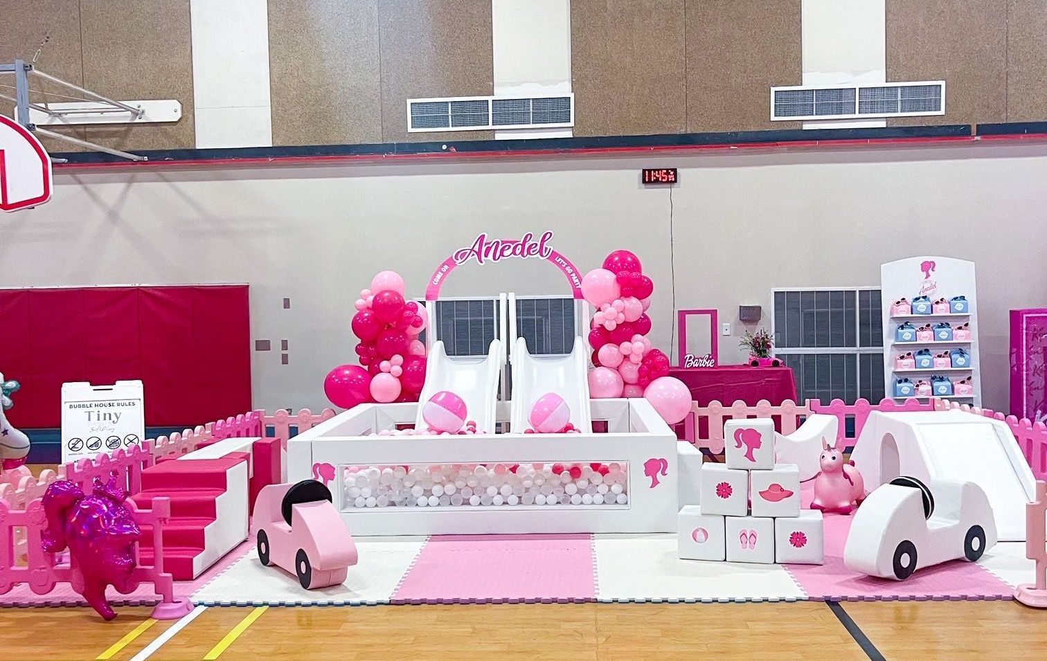 Pink balloon-decorated stage with a white arch and cartoon car props in a gymnasium