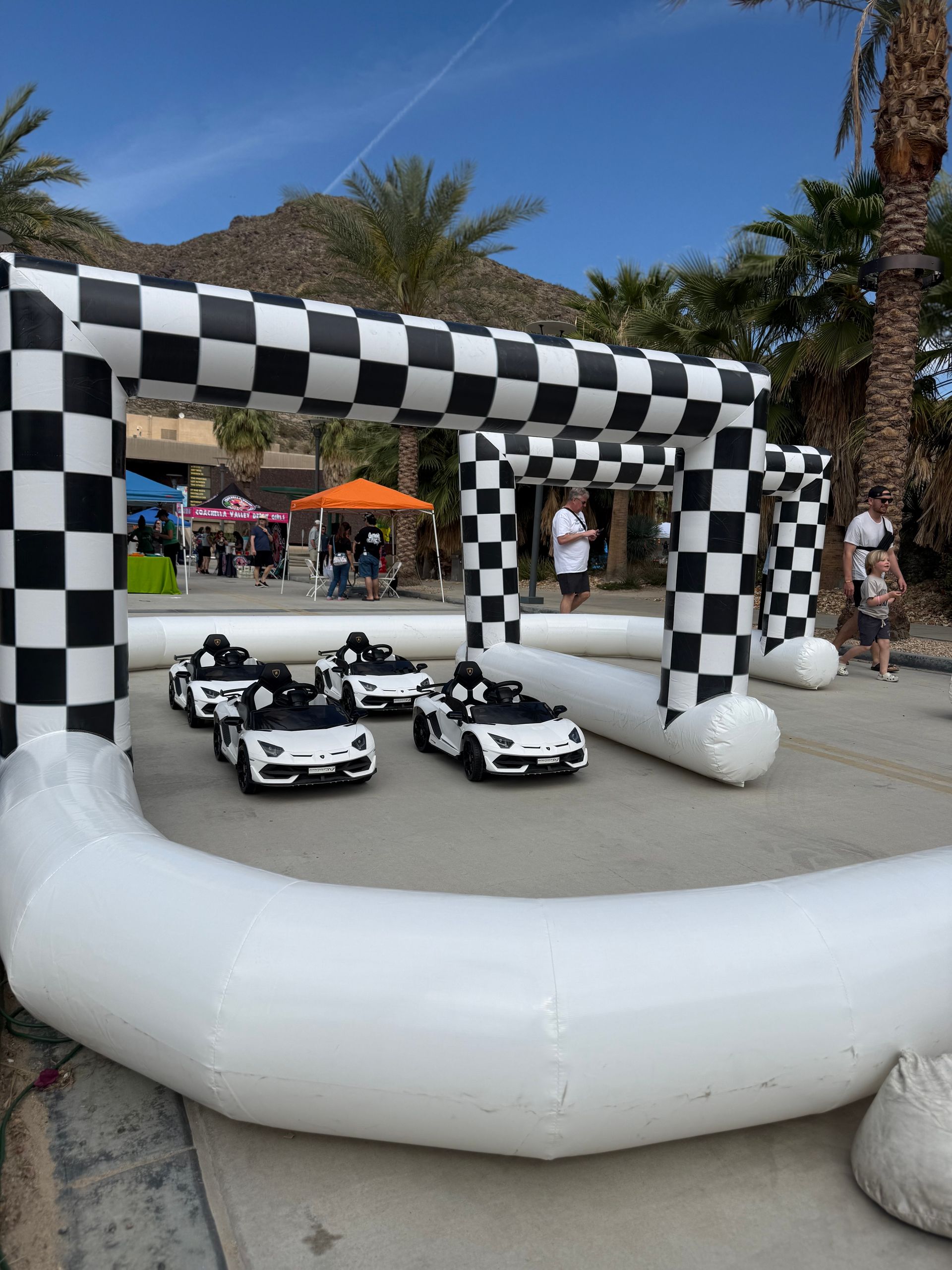 Checkered inflatable race track with several small white toy race cars outdoors