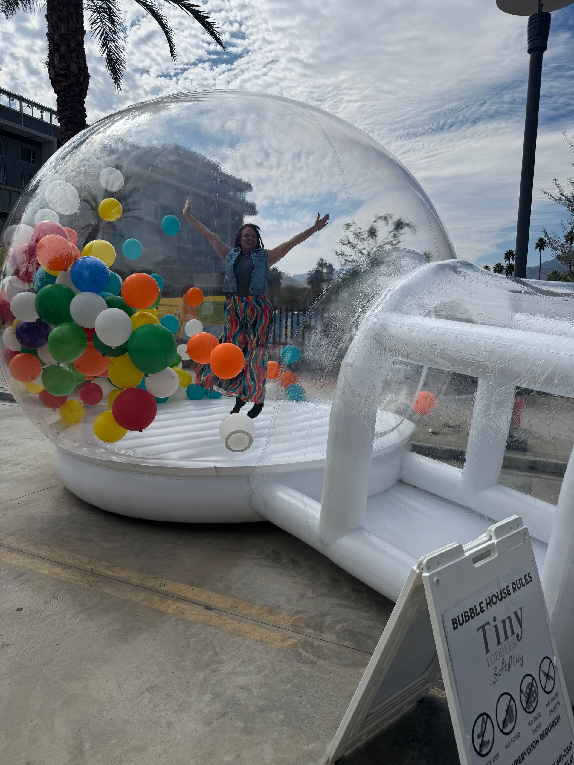 People inside a clear inflatable bubble with colorful balloons, beside an outdoor white inflatable structure.