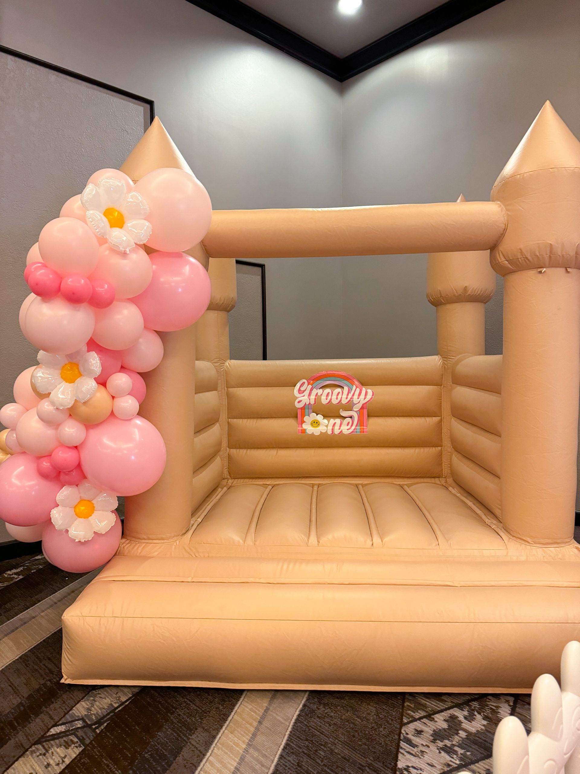 Tan inflatable bounce house with pink flower balloon arch in a room