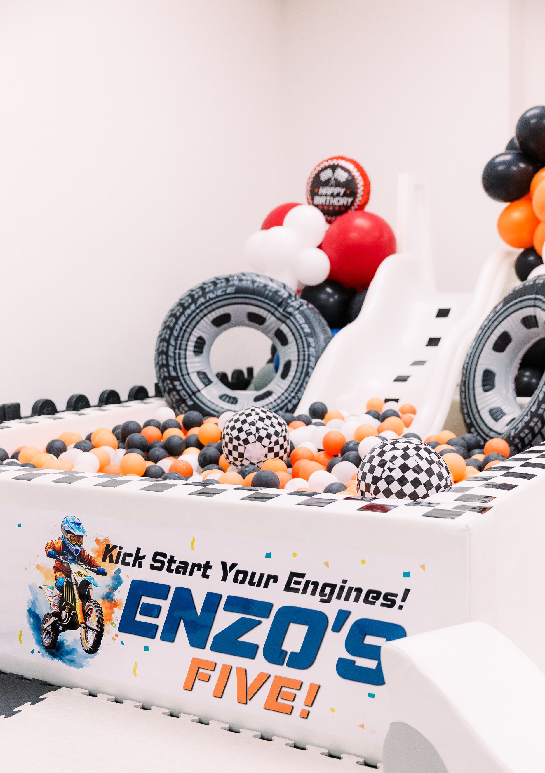 White-and-black balloon race-car birthday display with large tires and “ENZO’S FIVE!” banner