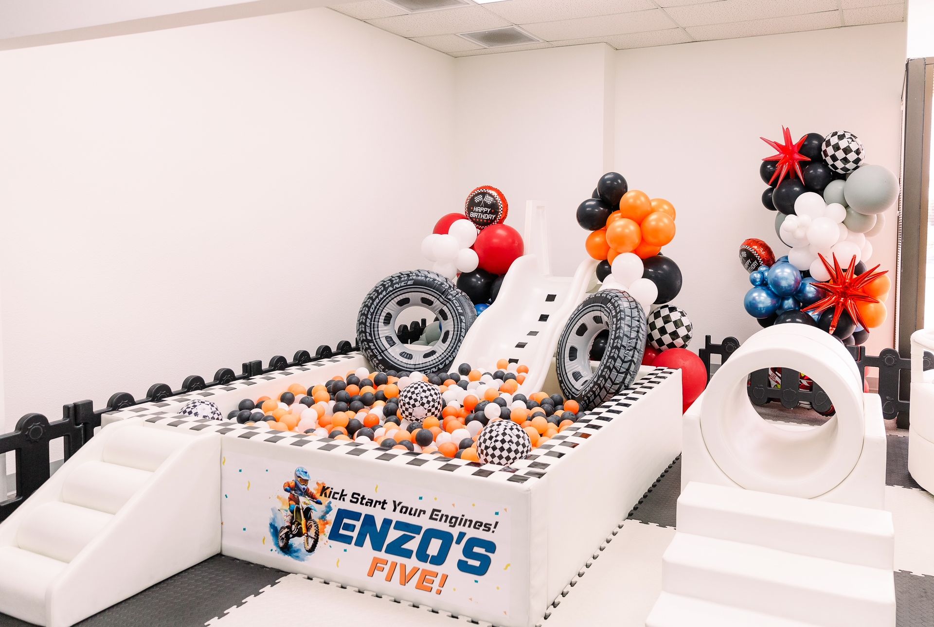 Balloon-decorated race car display on a white stage with ENZO’S logo and checkered accents