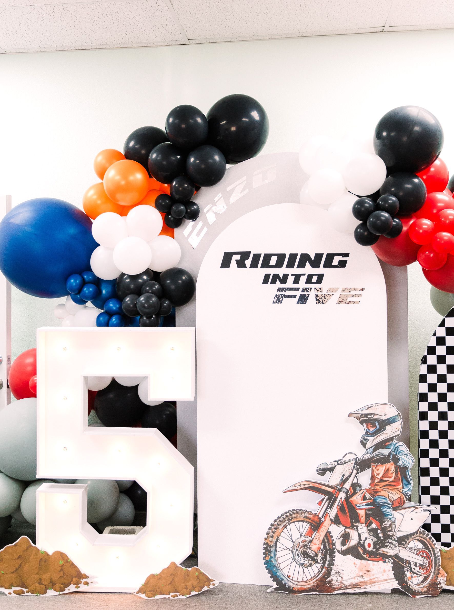 Motocross-themed display with balloons, a large white 5, and a rider graphic beside a white backdrop