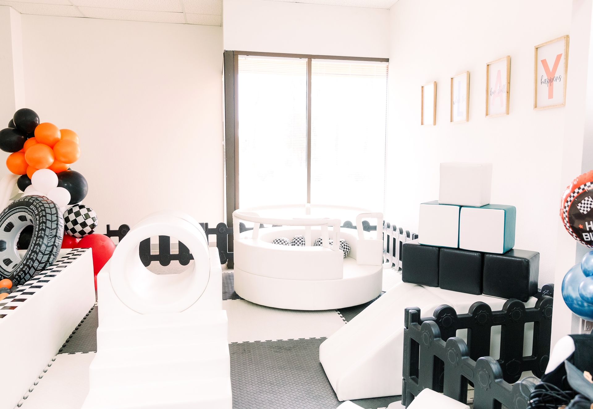Bright playroom with white-and-black ball pit, balloon decor, and minimalist furniture