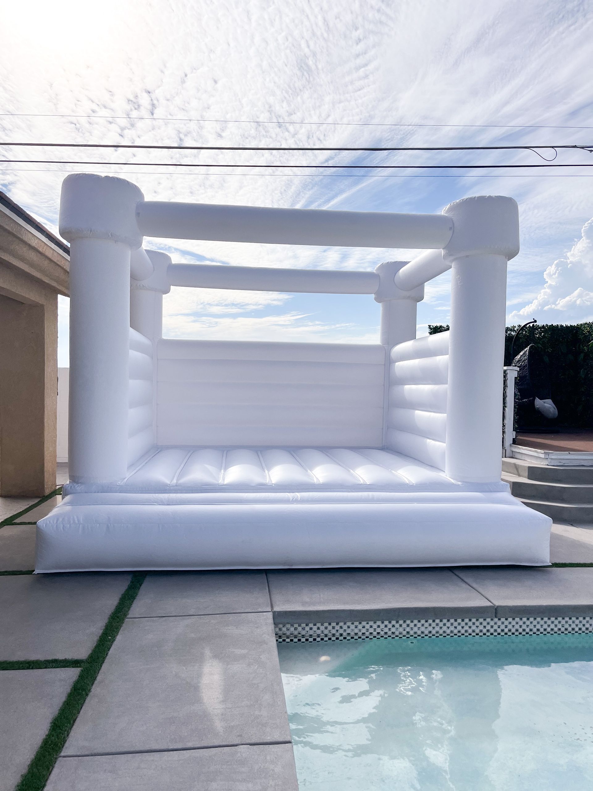 White inflatable bounce house beside a pool in a sunny backyard